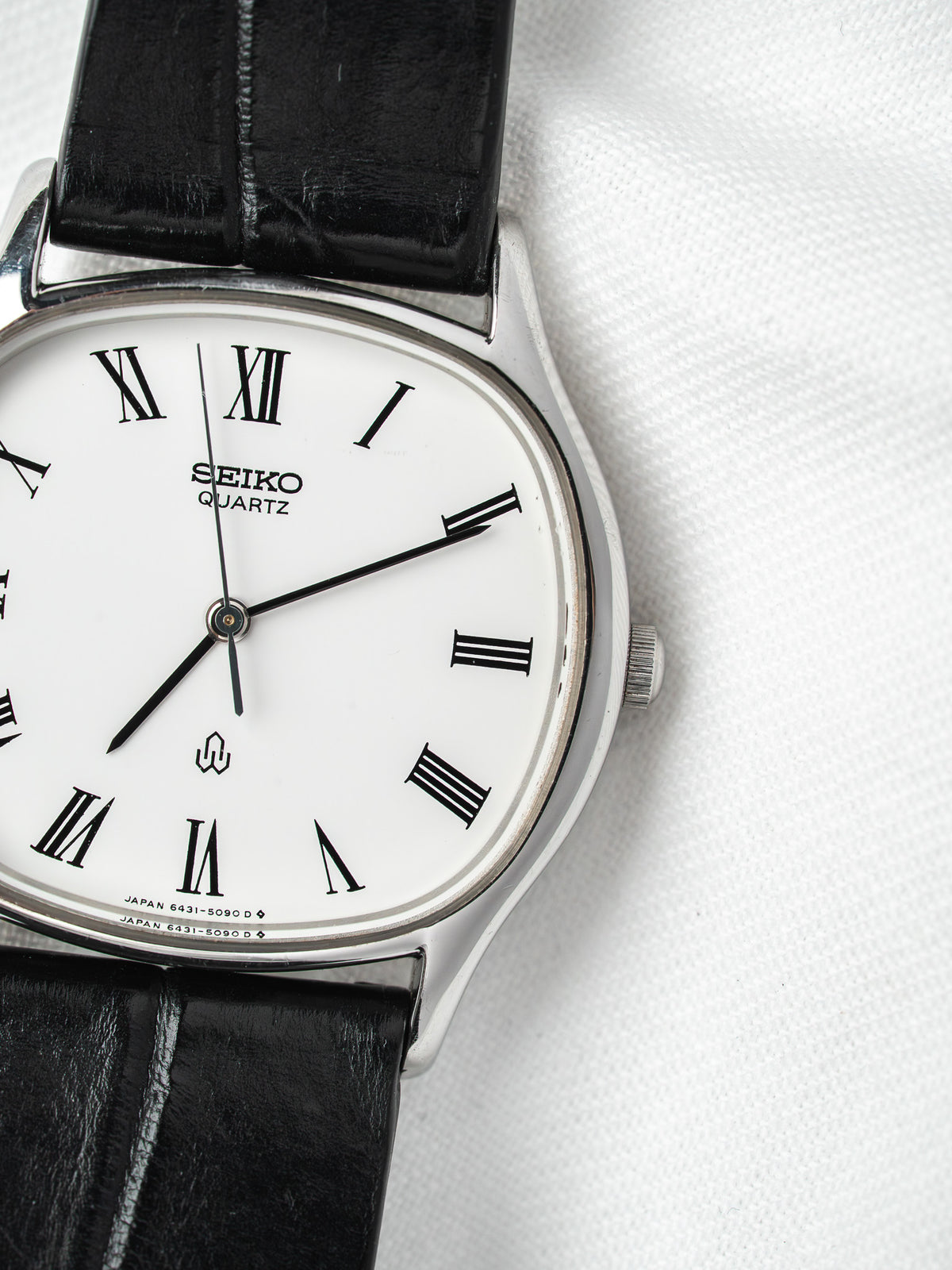 Seiko Quartz vintage watch with white dial, Roman numerals, black leather strap on white background