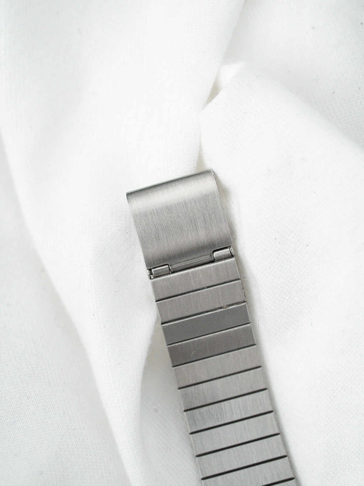 Détail du fermoir et du bracelet en acier inoxydable posés sur un tissu blanc.