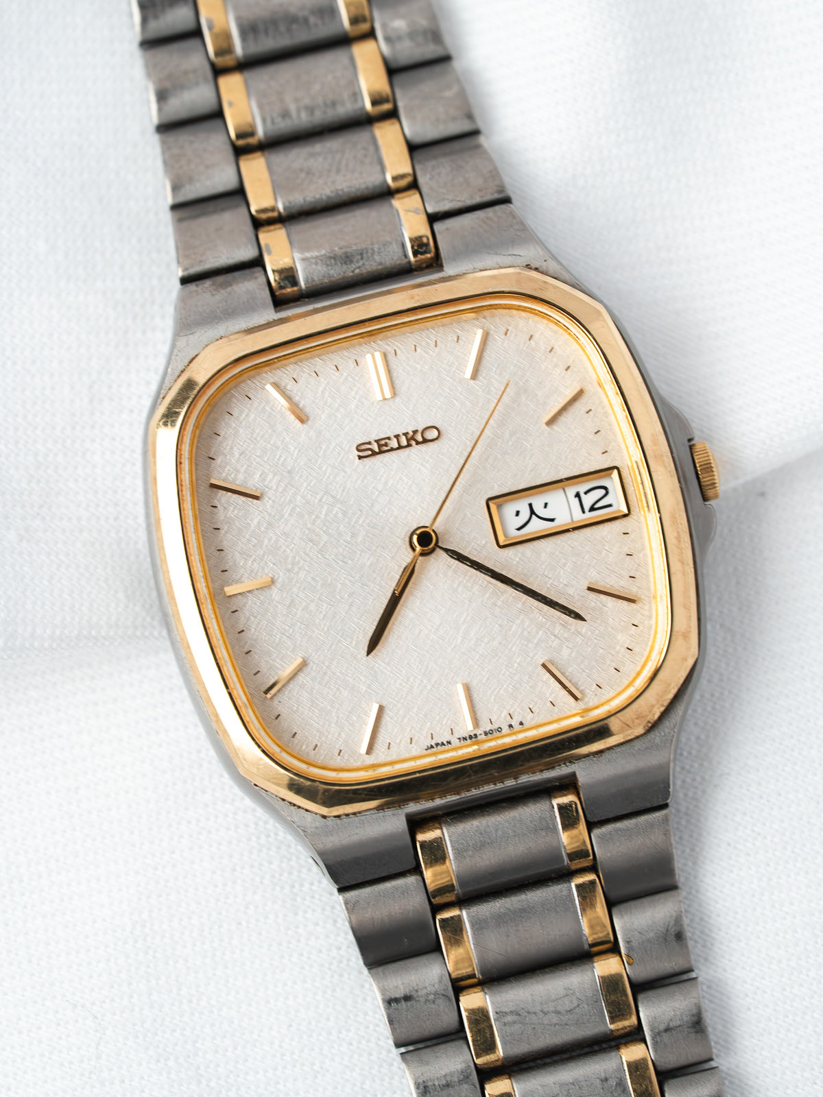 Seiko vintage watch with gold-toned bezel, silver dial, and two-tone bracelet on white background