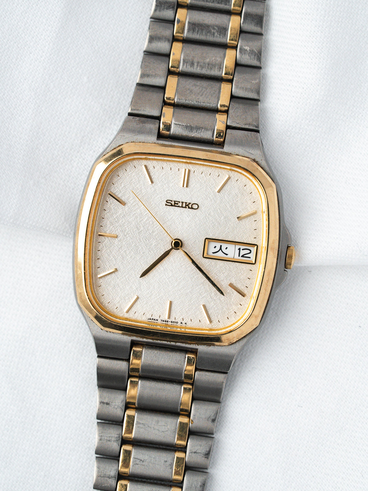 Seiko vintage watch with gold-tone bezel, silver dial, and two-tone bracelet on white background