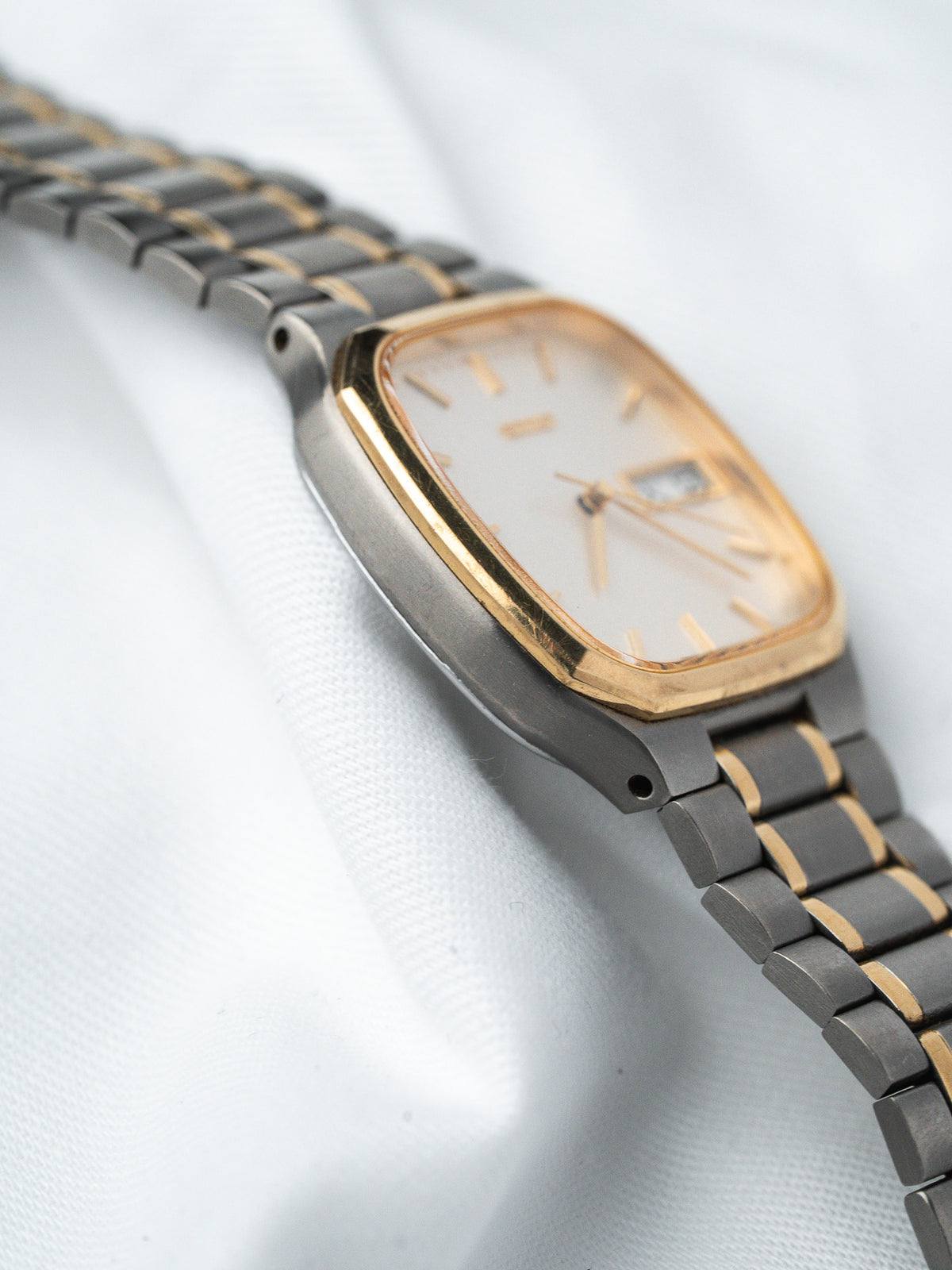 Vintage Omega watch with gold bezel, silver dial, and two-tone bracelet on white fabric