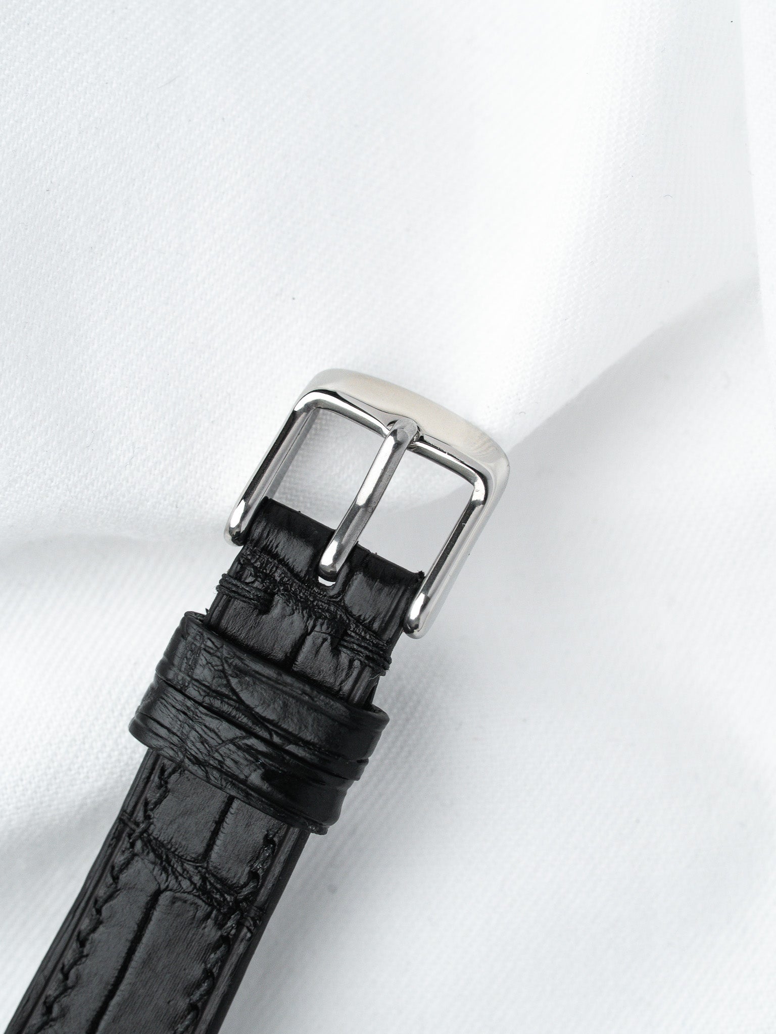 Black alligator leather watch strap with polished steel buckle on white fabric