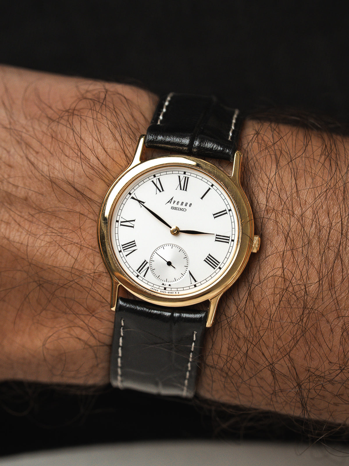 Montre Seiko Avenue vintage, boîtier doré, cadran blanc et bracelet cuir noir au poignet
