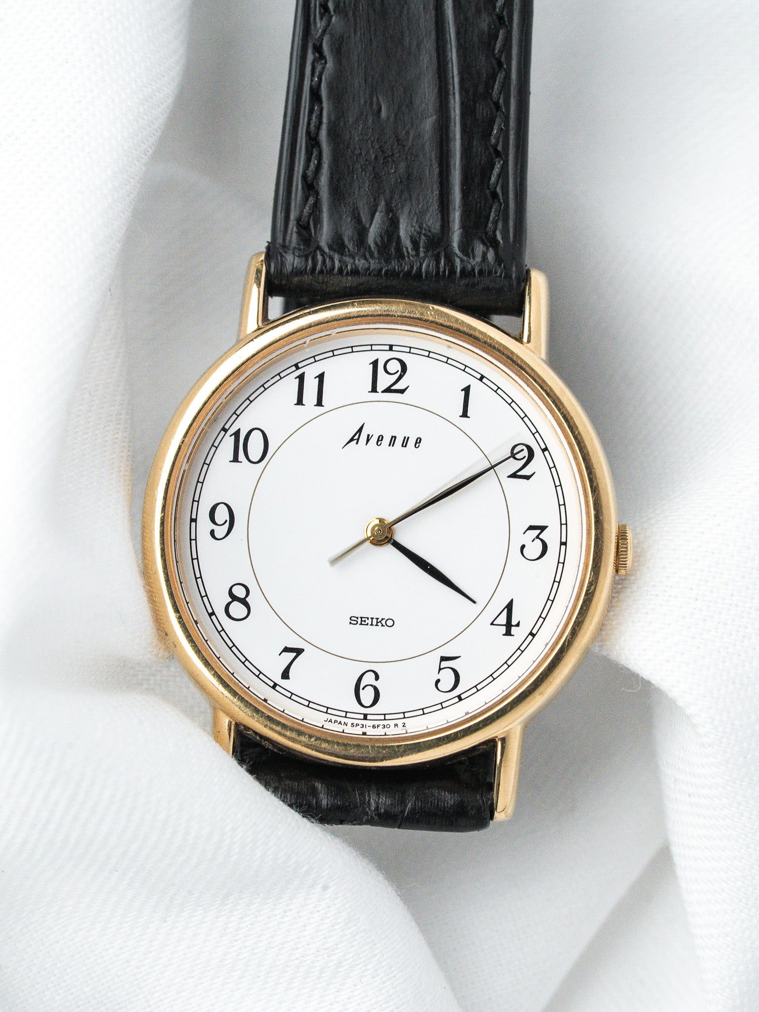 Seiko Avenue vintage watch with gold case, white dial, black leather strap on white fabric