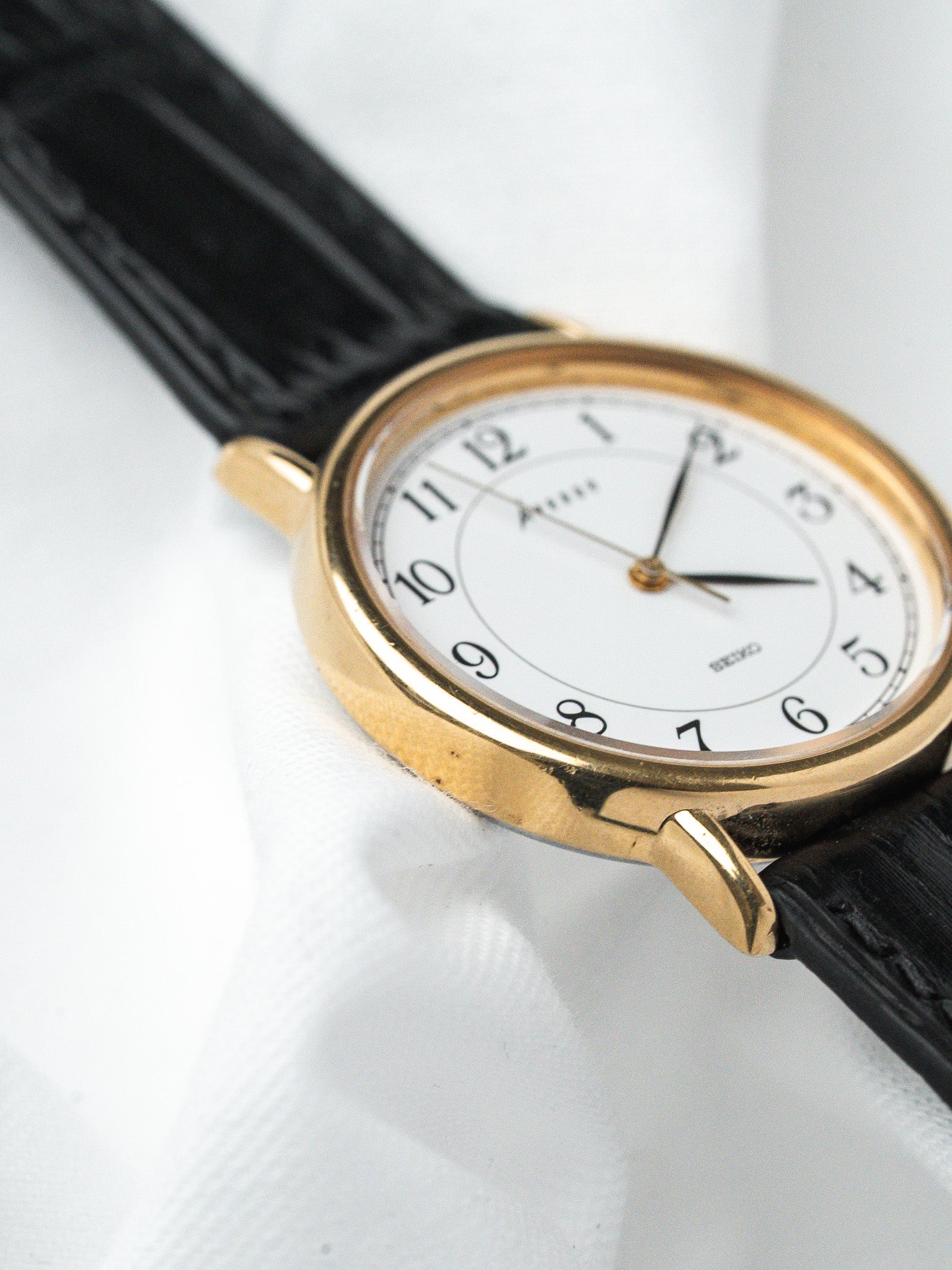 Seiko vintage watch with gold case, white dial, black leather strap on white background