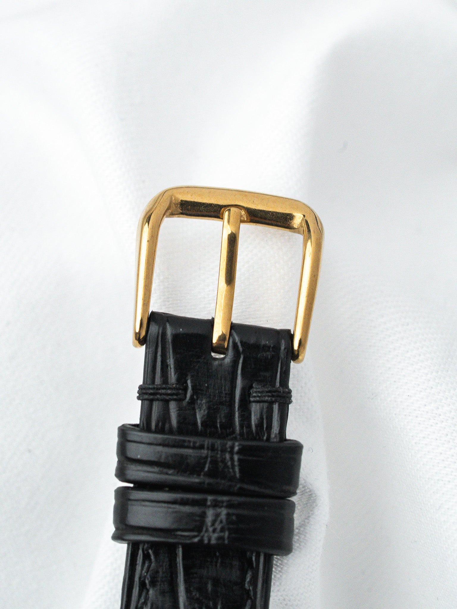 Black alligator leather watch strap with gold-toned buckle on white background