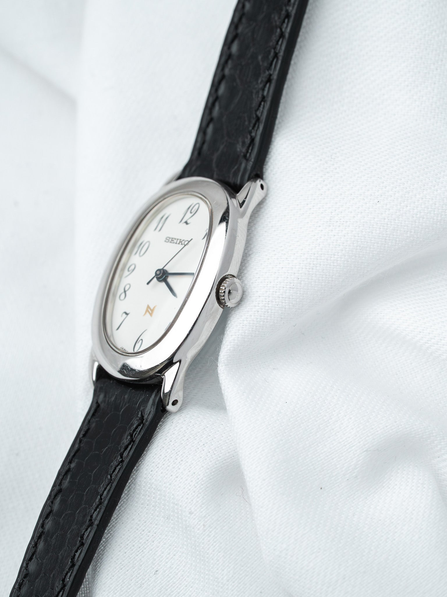 Seiko vintage watch with white dial, black leather strap, silver case on white fabric