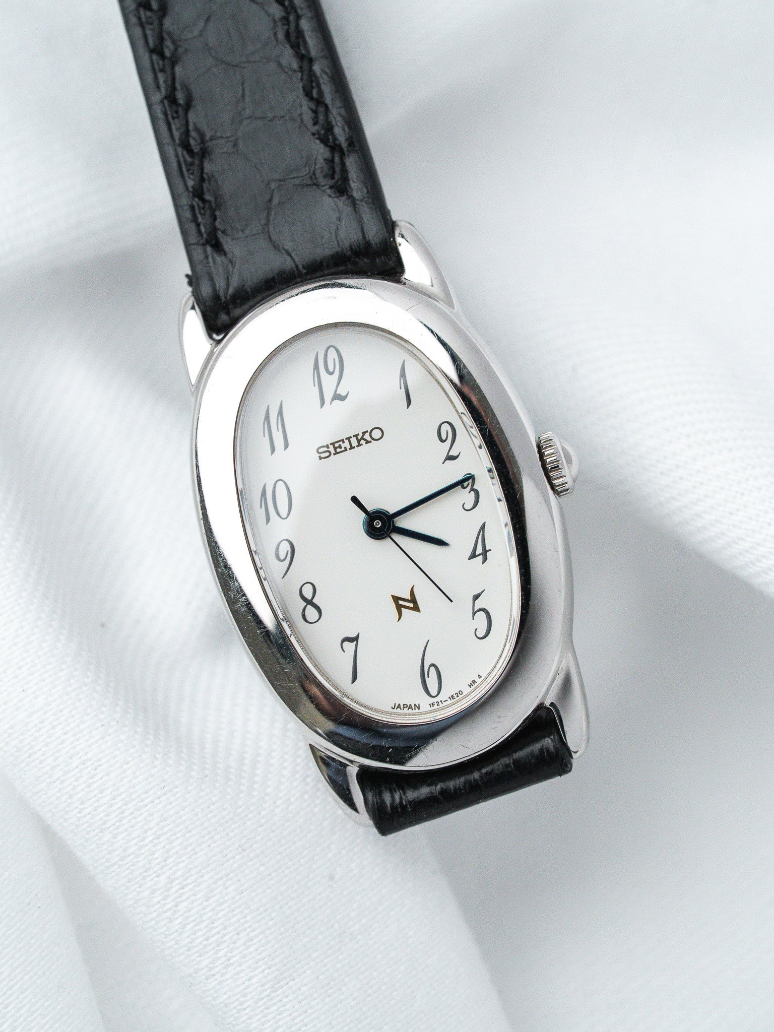 Seiko vintage watch with white dial, black leather strap, and silver case on white fabric