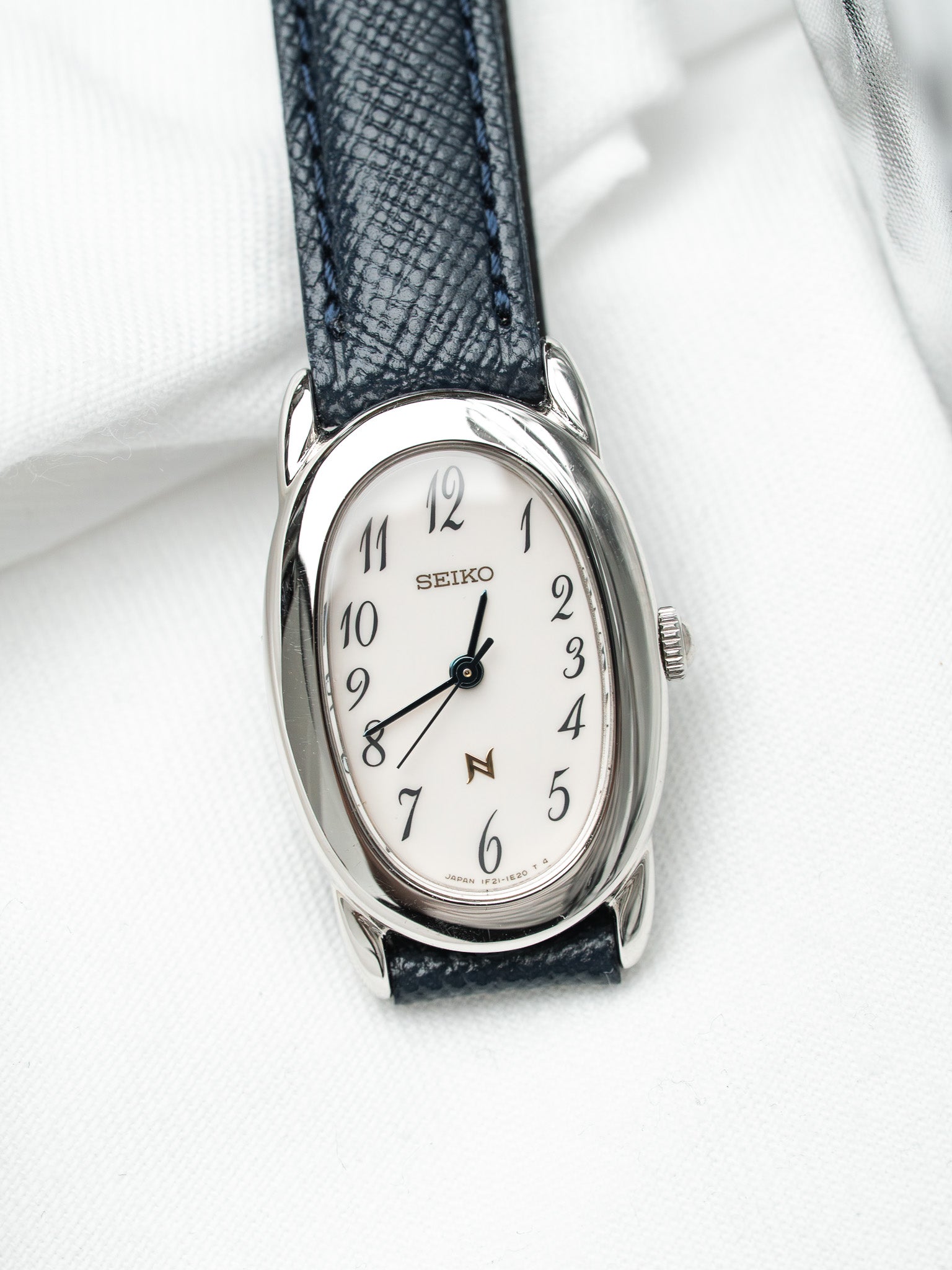 Seiko vintage watch with white dial, blue leather strap, and silver case on white fabric