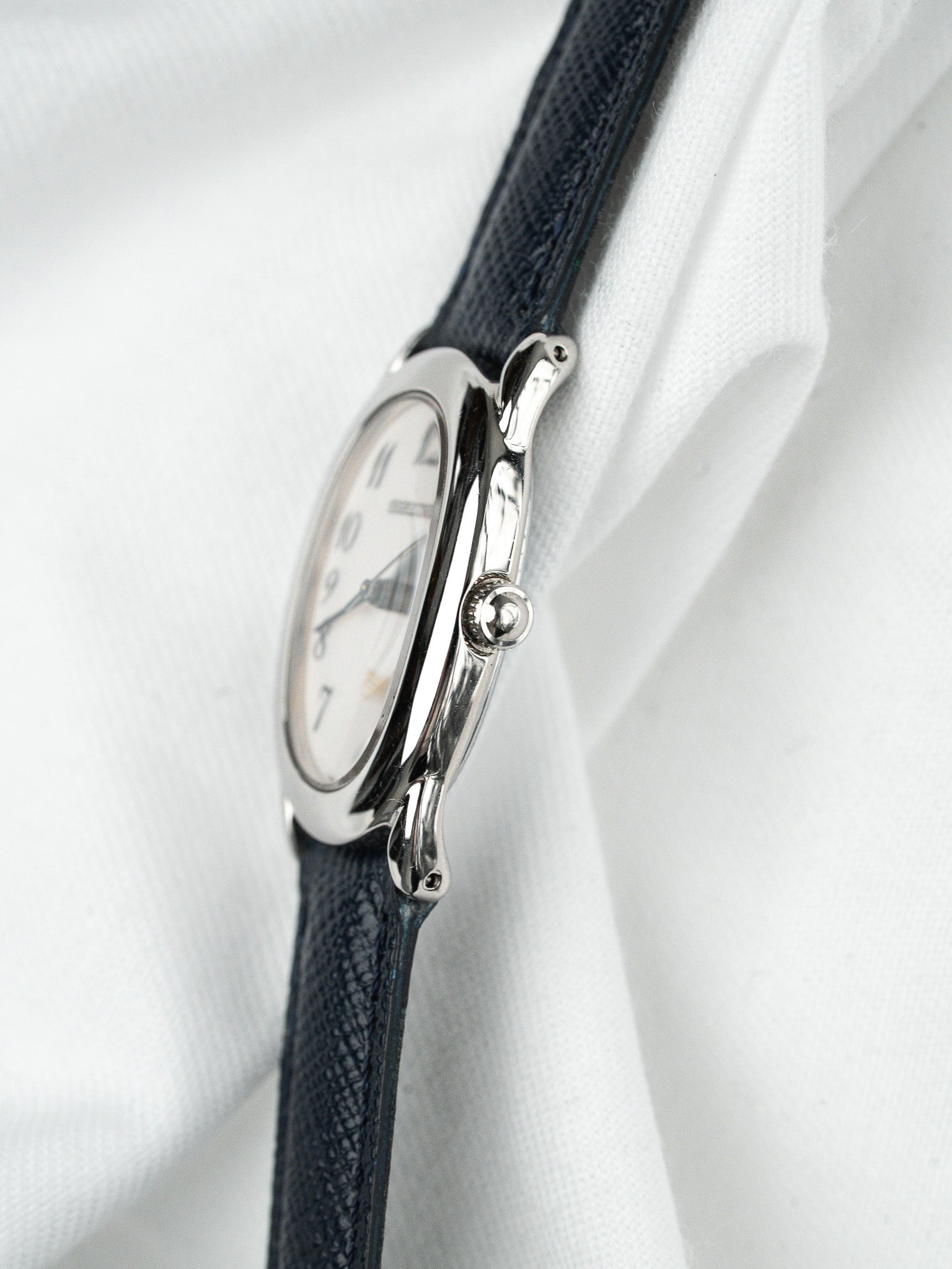 Cartier vintage watch with white dial, steel case, and dark leather strap on white fabric