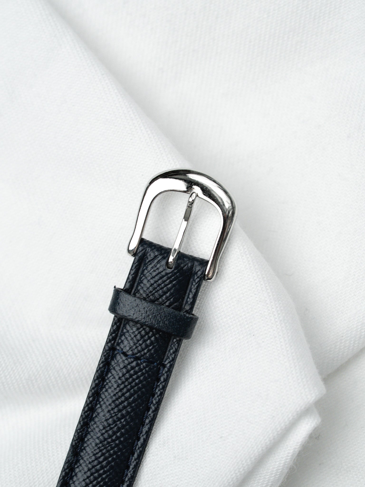 Black textured leather watch strap with polished steel buckle on white fabric