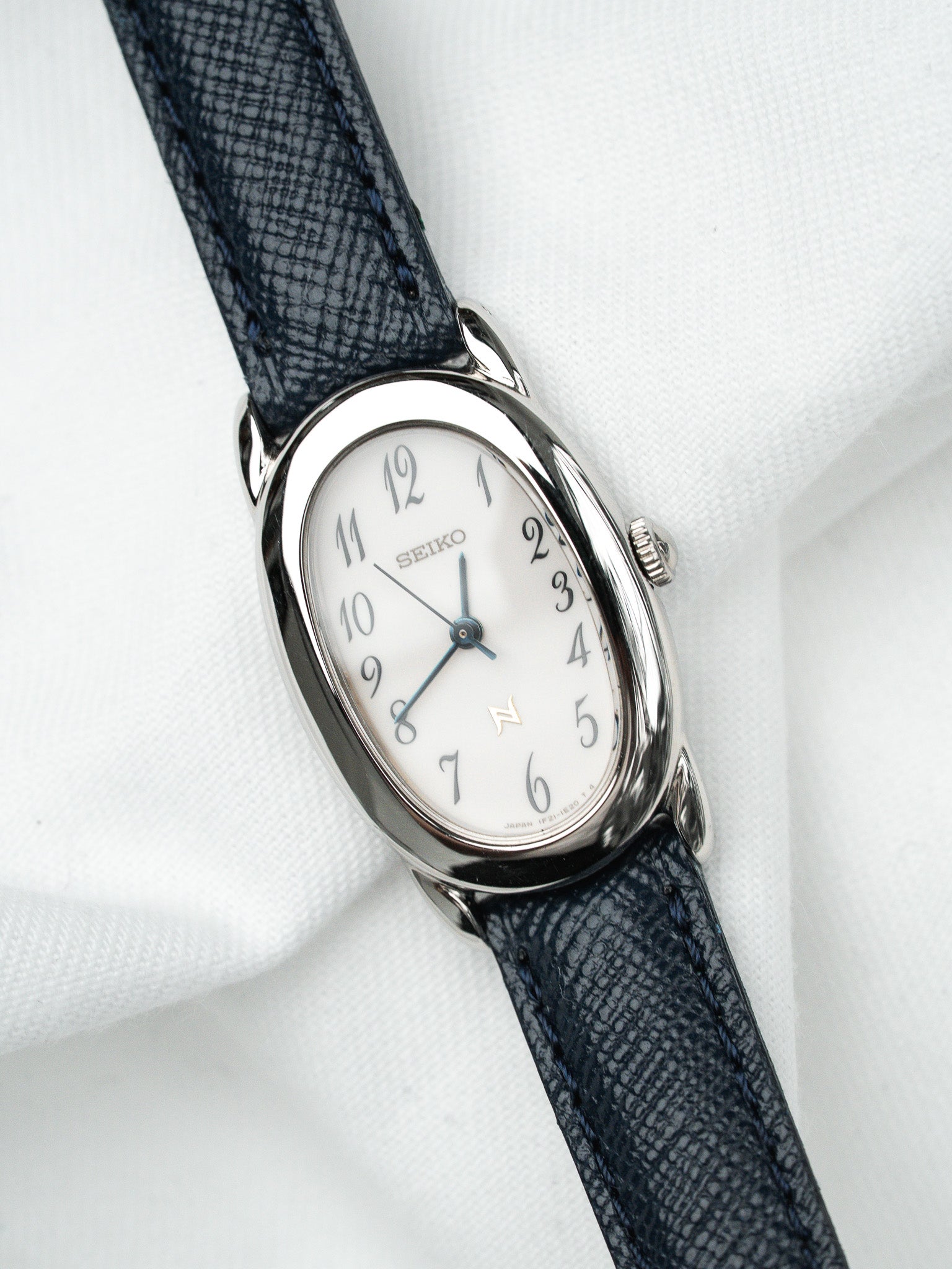 Seiko vintage watch with white dial, blue hands, and dark blue textured strap on white fabric