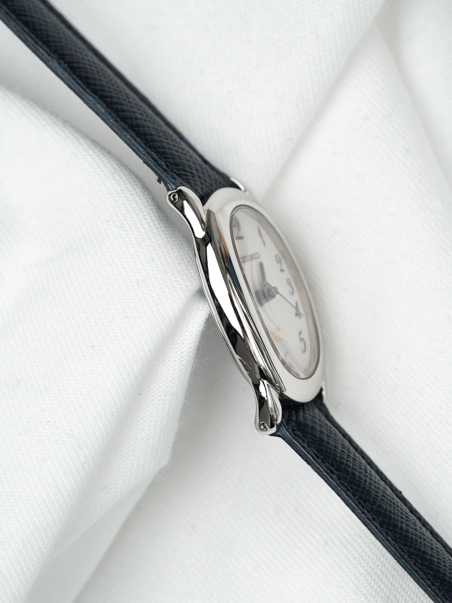 Seiko vintage watch with silver case, white dial, and dark blue leather strap on white fabric