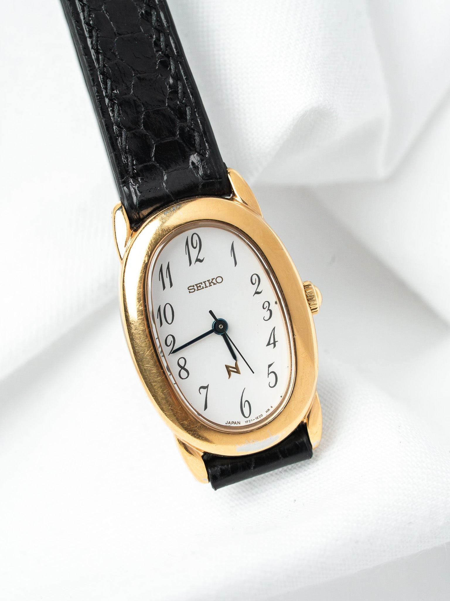 Seiko vintage watch with gold oval case, white dial, black crocodile strap on white fabric