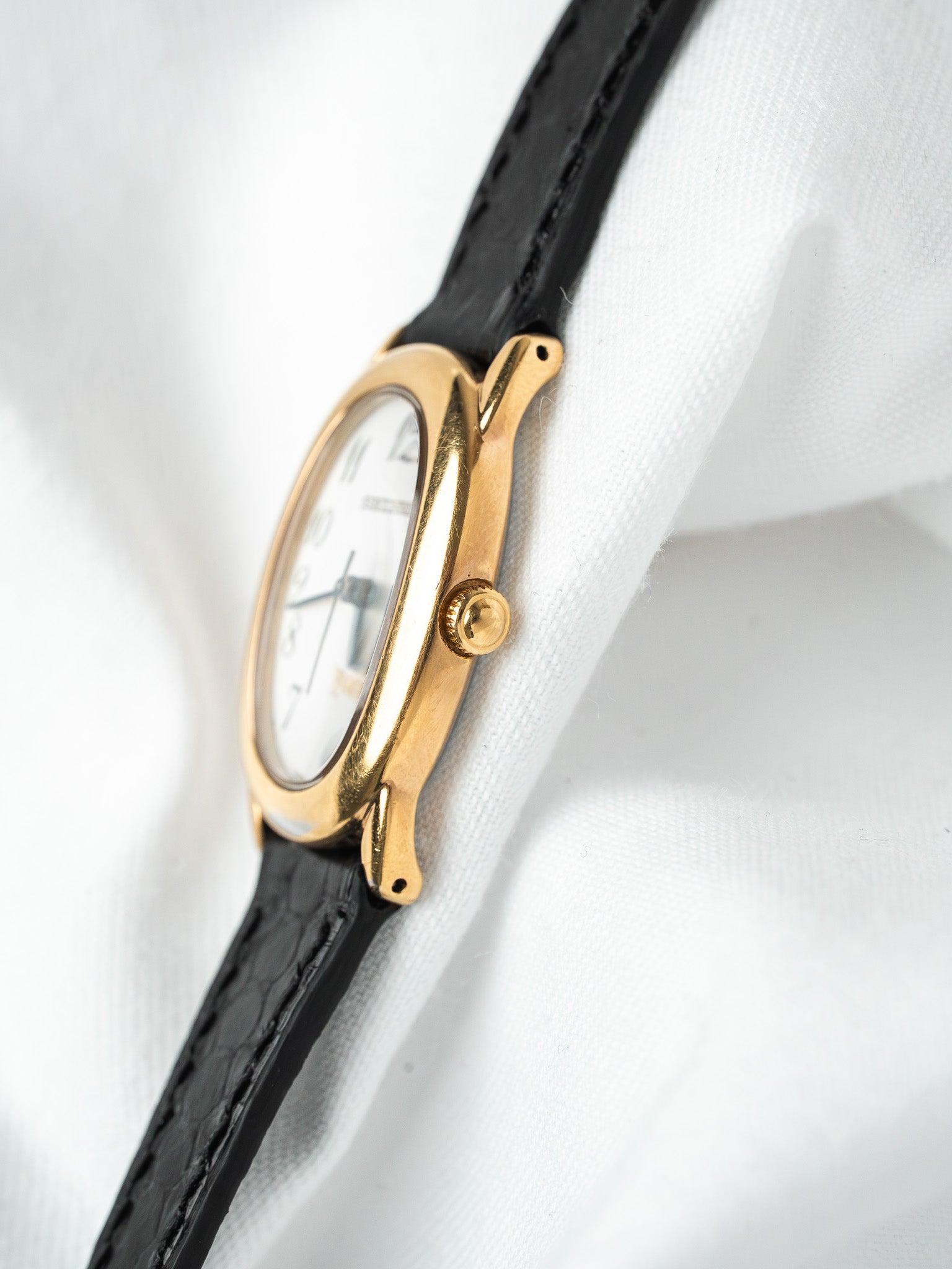 Cartier vintage watch with gold case, white dial, black leather strap on white fabric