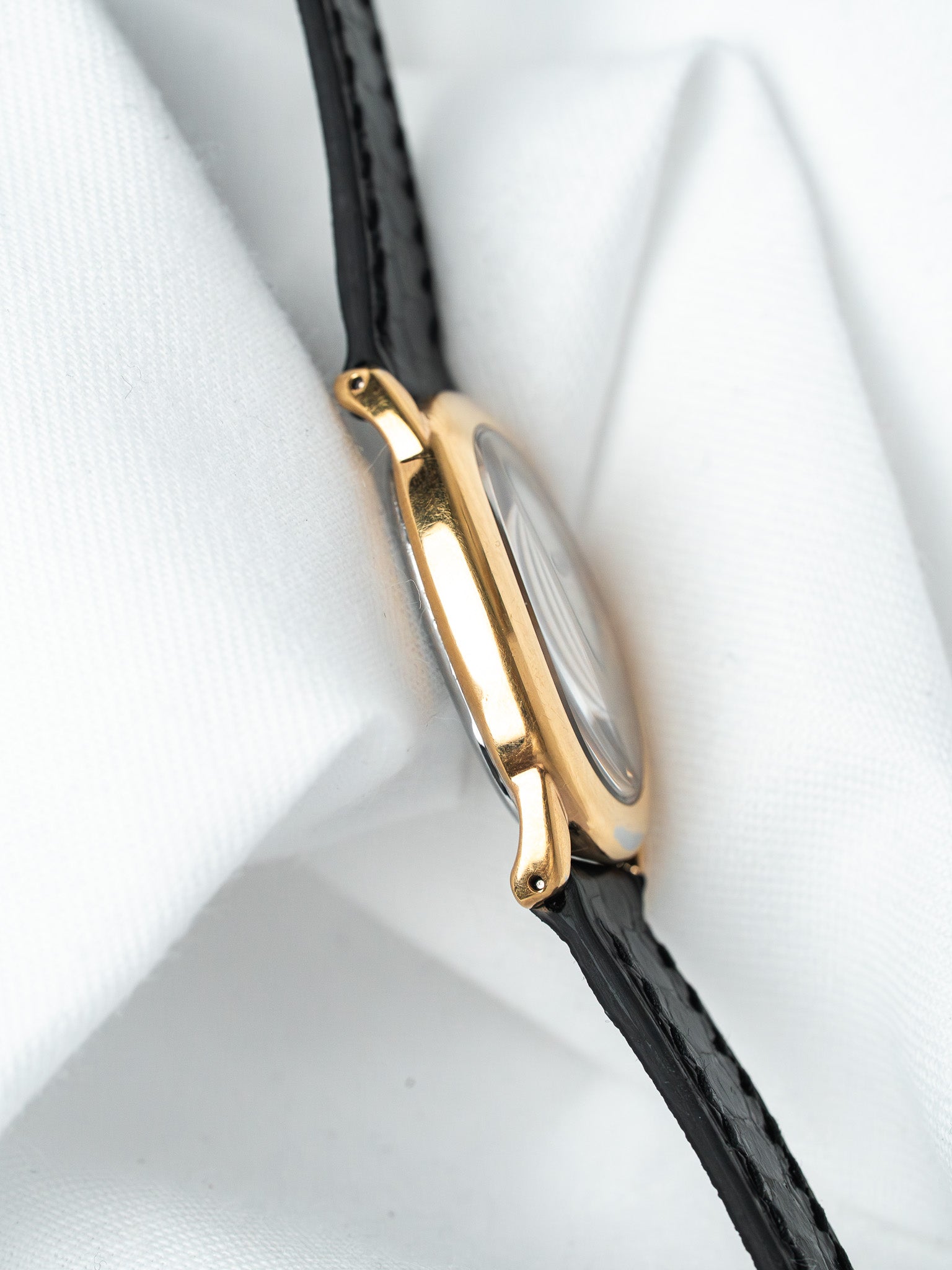 Vintage Cartier watch with gold case and black leather strap on white fabric