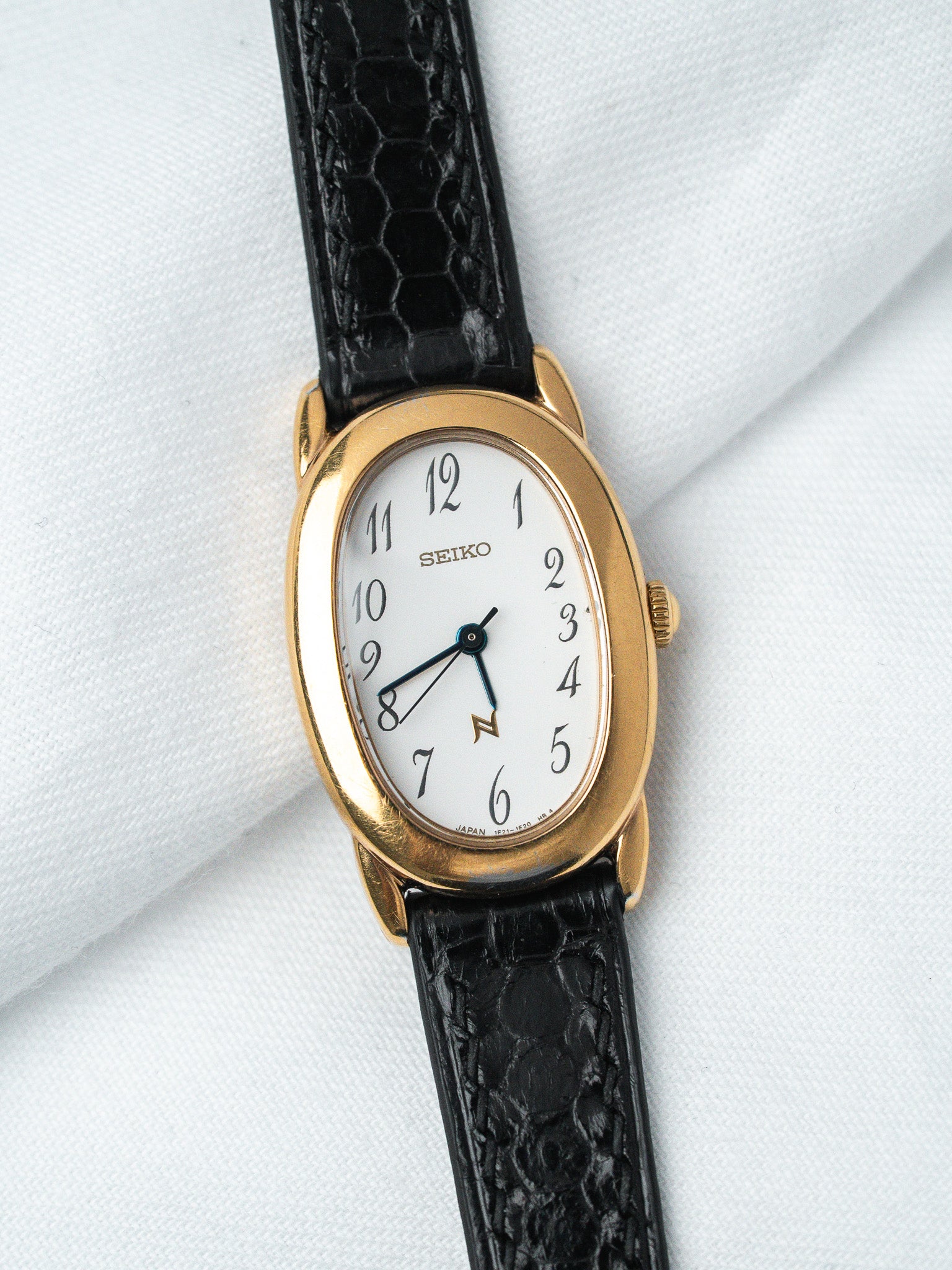 Seiko vintage watch with gold case, white dial, black leather strap on white fabric