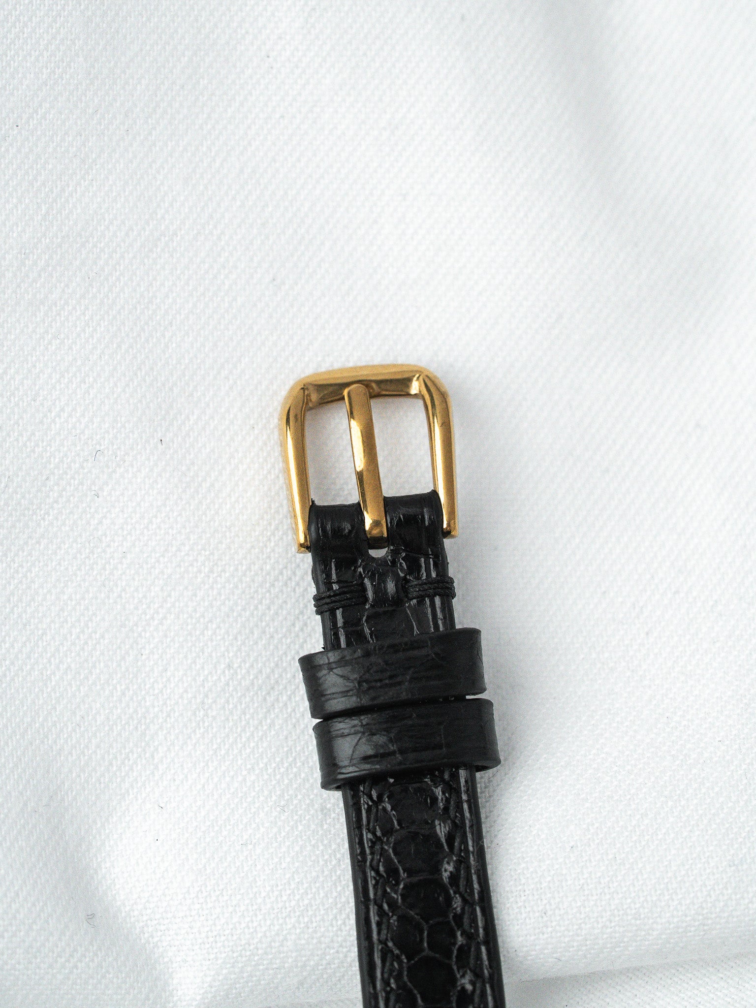 Black alligator leather watch strap with gold buckle on white background