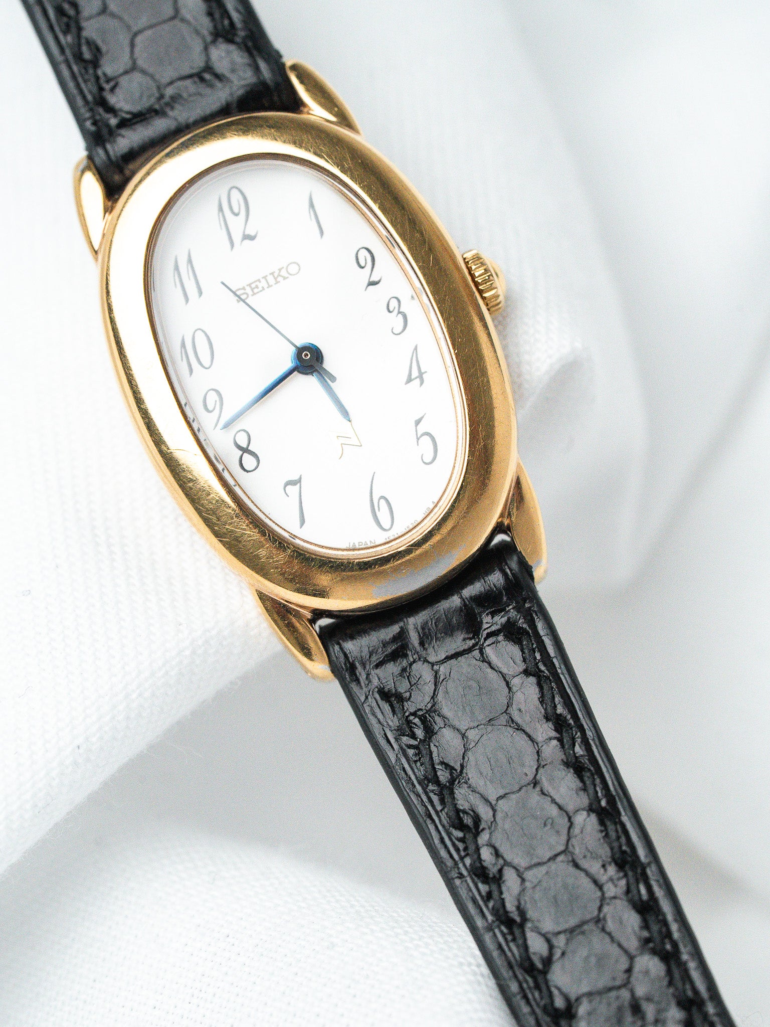 Seiko vintage watch with gold oval case, white dial, blue hands, black crocodile strap