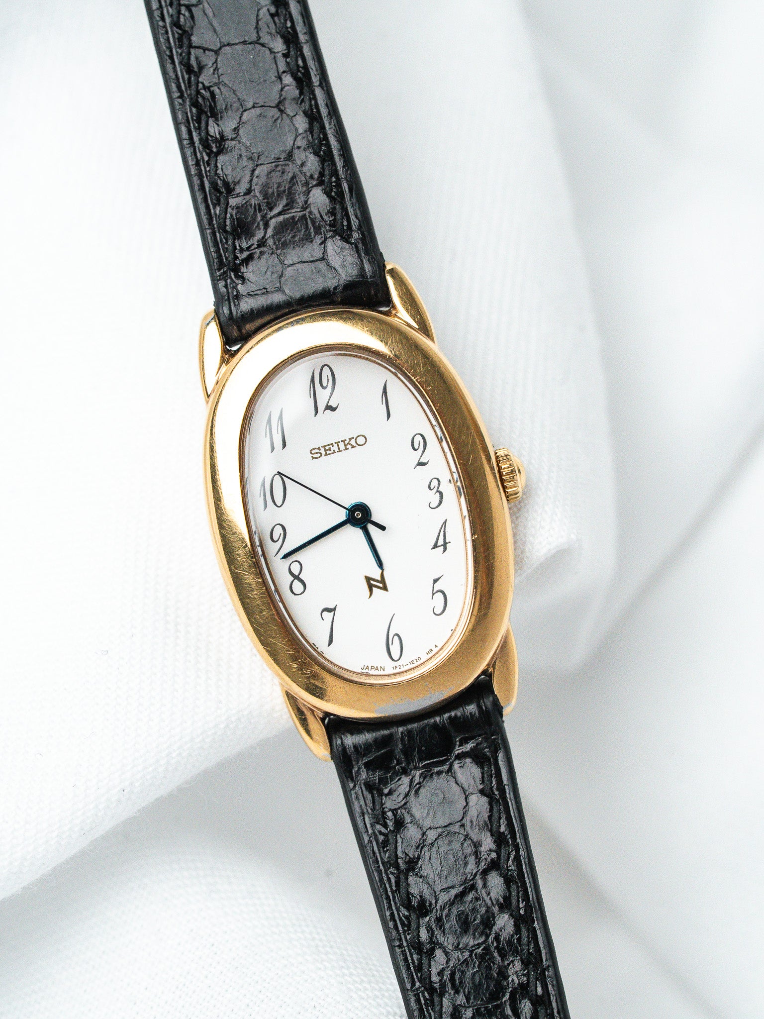Seiko vintage watch with gold case, white dial, black alligator strap on white background
