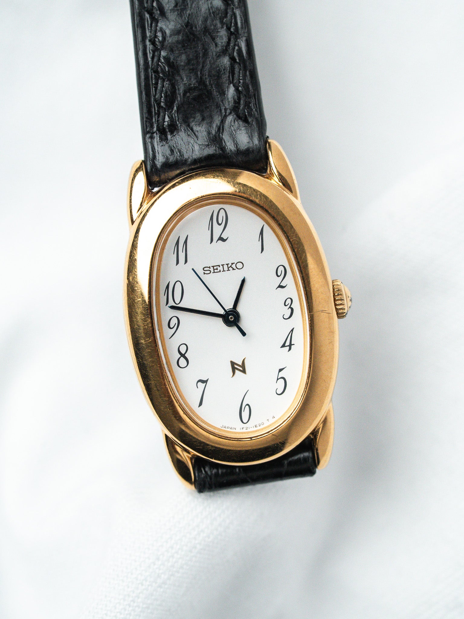 Seiko vintage watch with gold case, white dial, black leather strap on white background