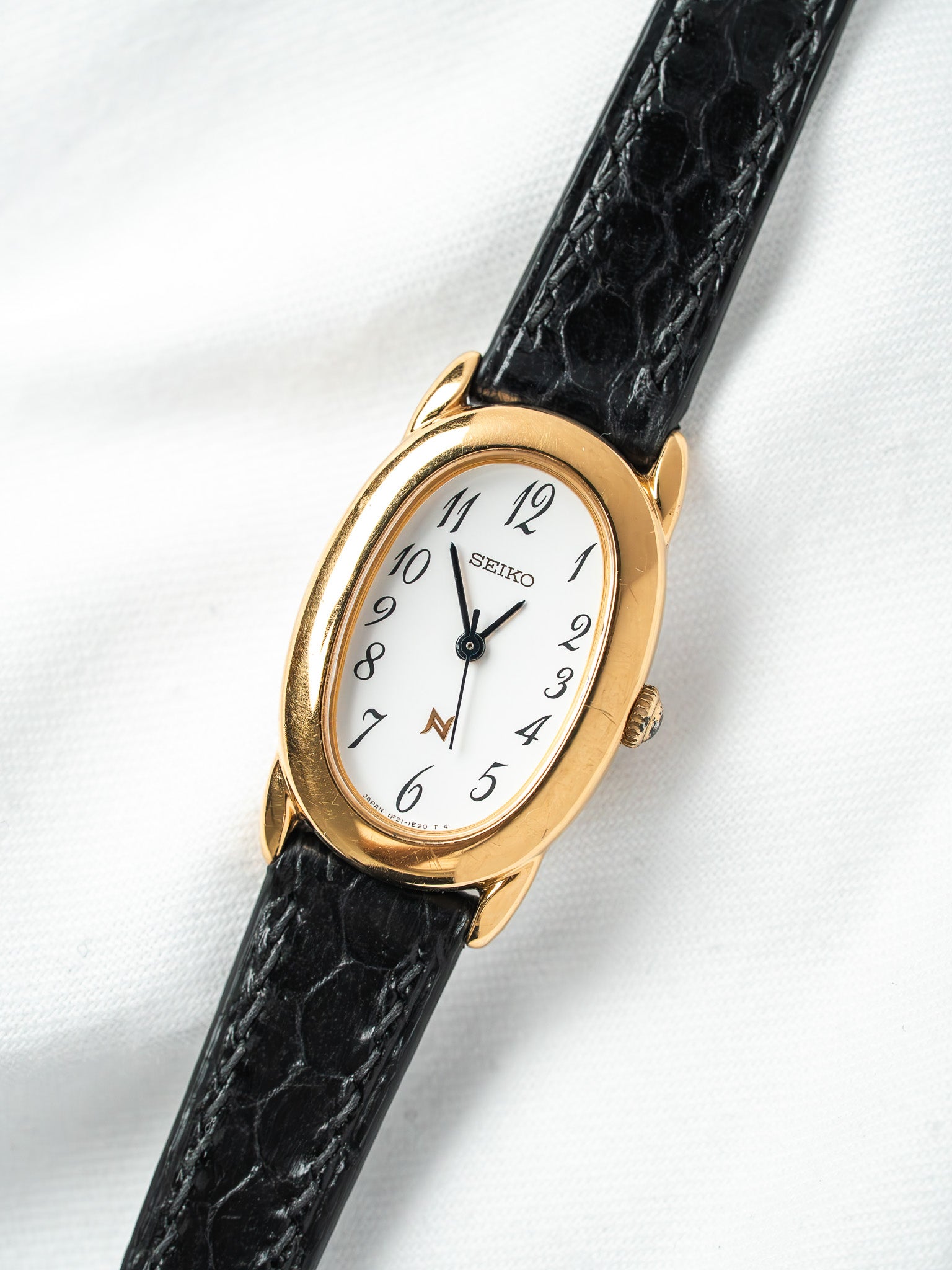 Seiko vintage watch with gold oval case, white dial, black alligator strap on white background