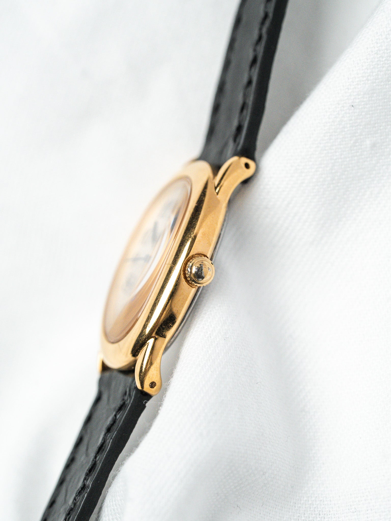 Vintage Cartier watch with gold case and black leather strap on white fabric