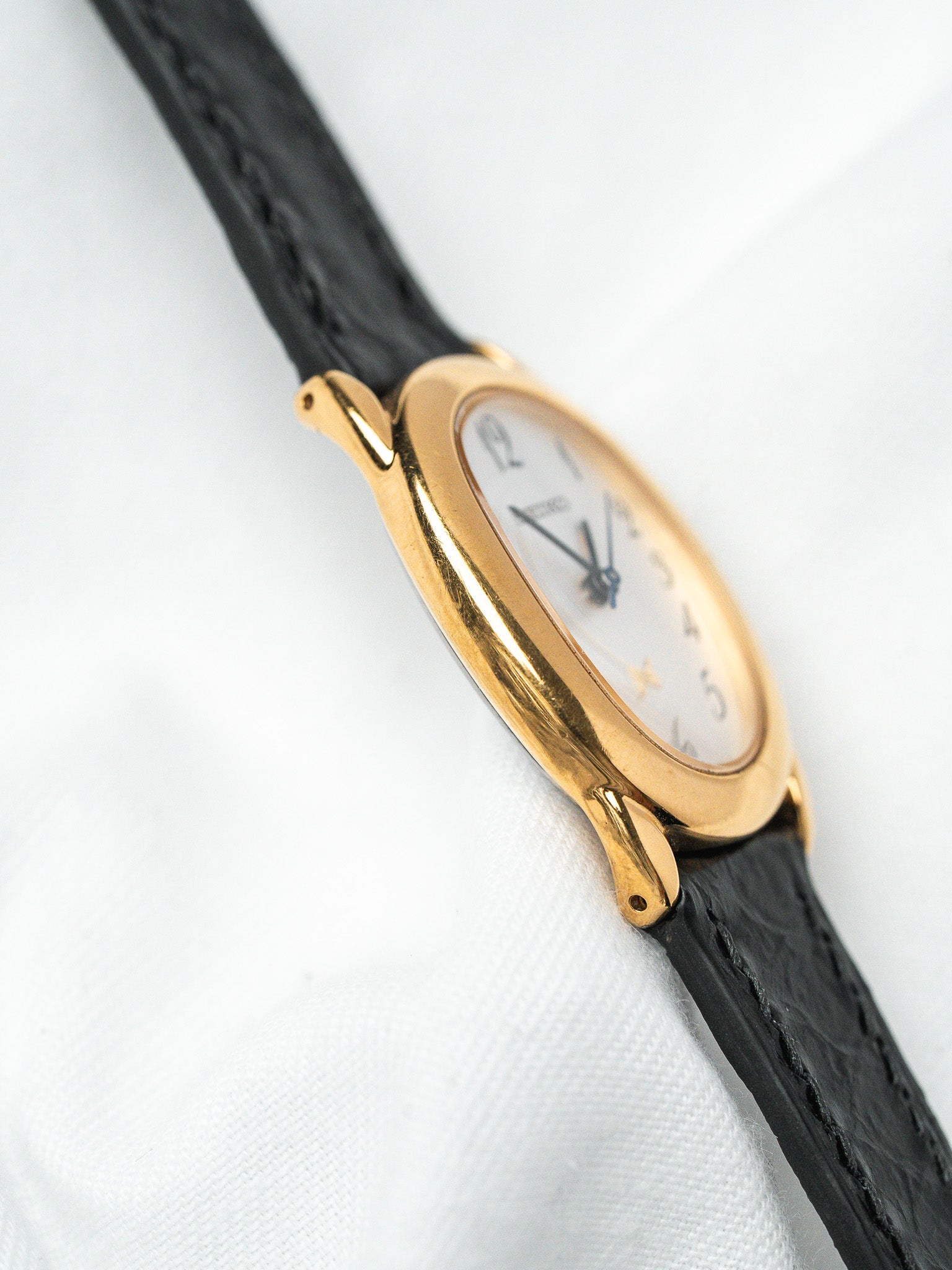 Vintage Cartier watch with gold case, white dial, black leather strap on white fabric