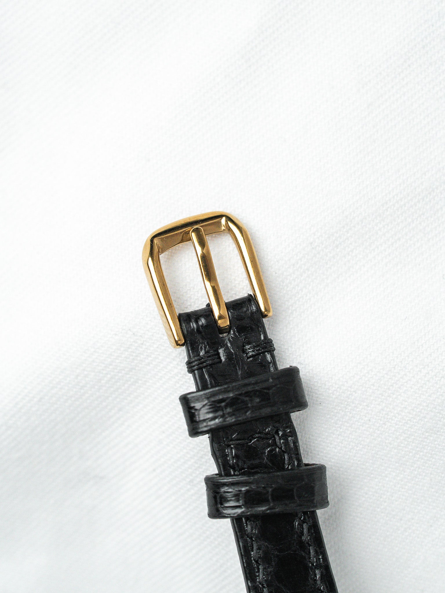 Black alligator leather watch strap with gold buckle on white background