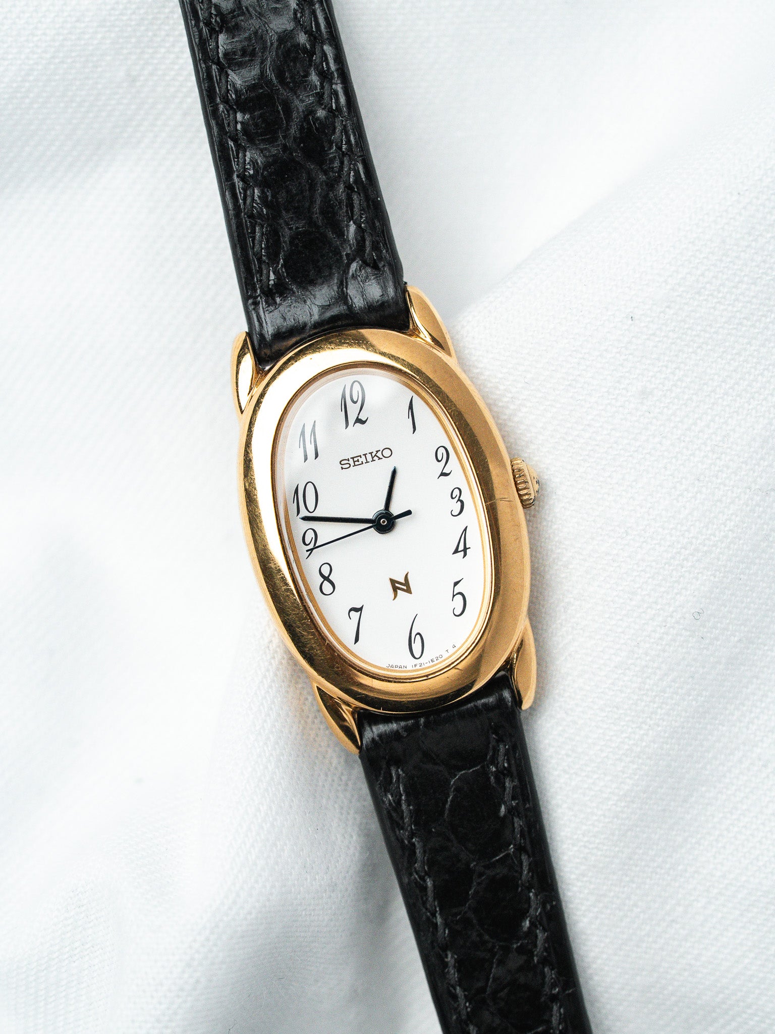 Seiko vintage watch with gold case, white dial, black alligator strap on white background