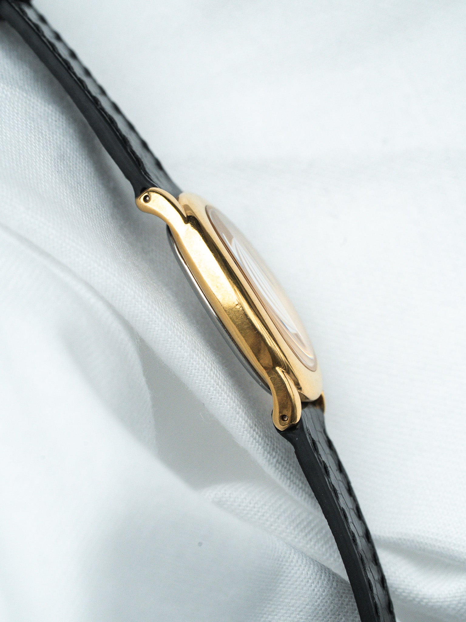 Vintage Cartier watch with gold case and black leather strap on white fabric