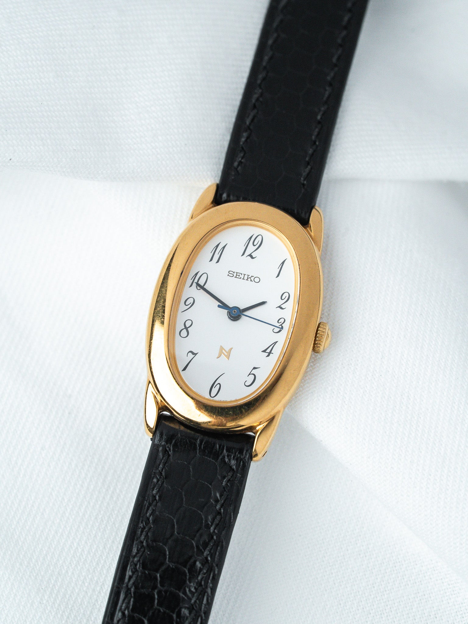 Seiko vintage watch with gold case, white dial, black leather strap on white background