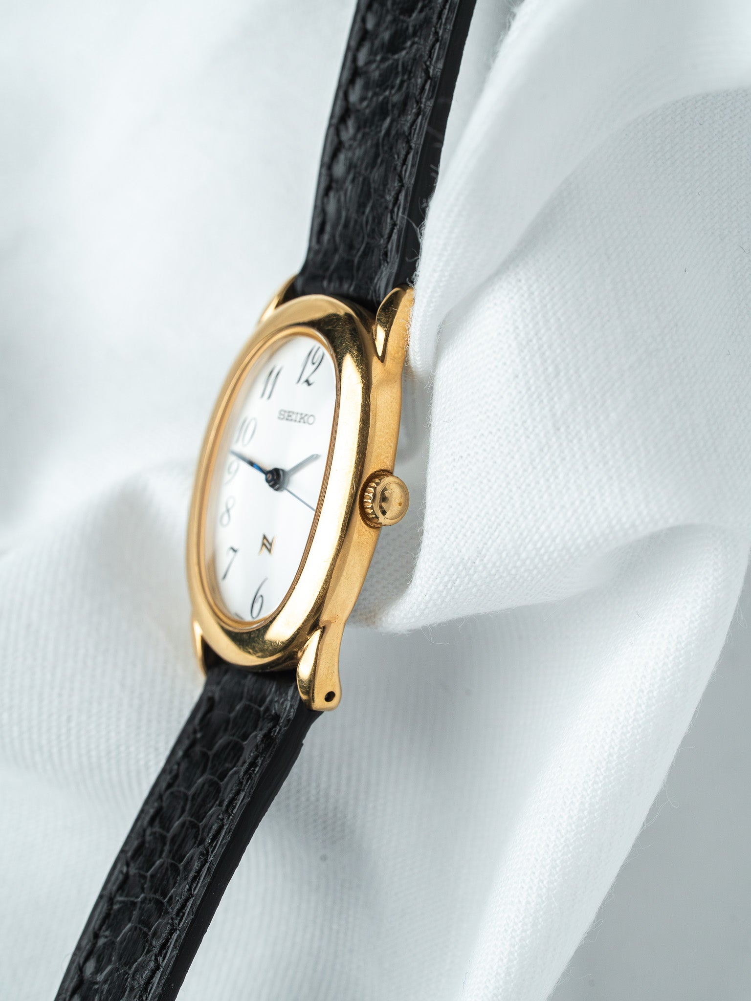 Seiko vintage watch with gold case, white dial, black leather strap on white fabric