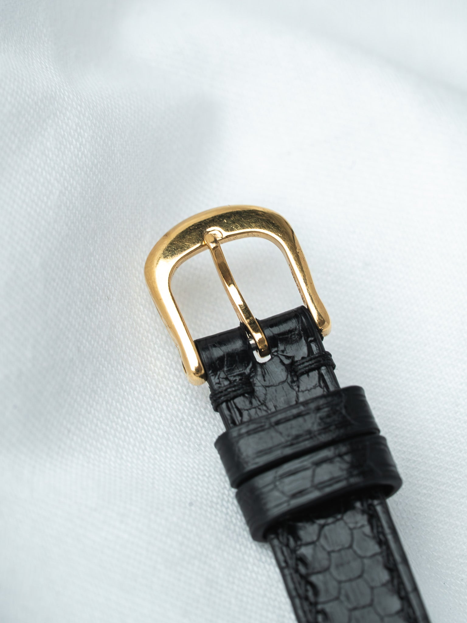 Black alligator leather watch strap with gold buckle on white fabric