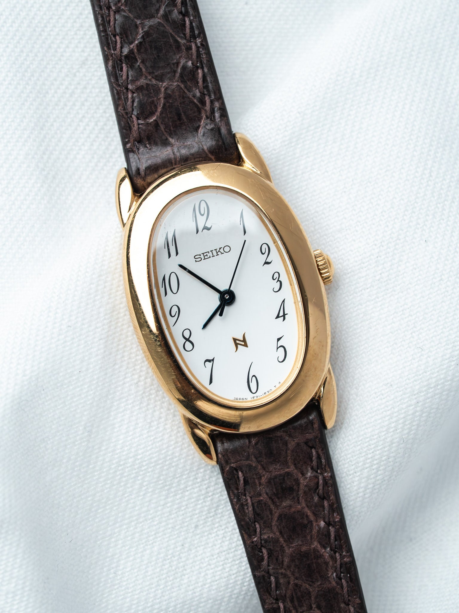 Seiko vintage watch with gold case, white dial, brown alligator strap on white background