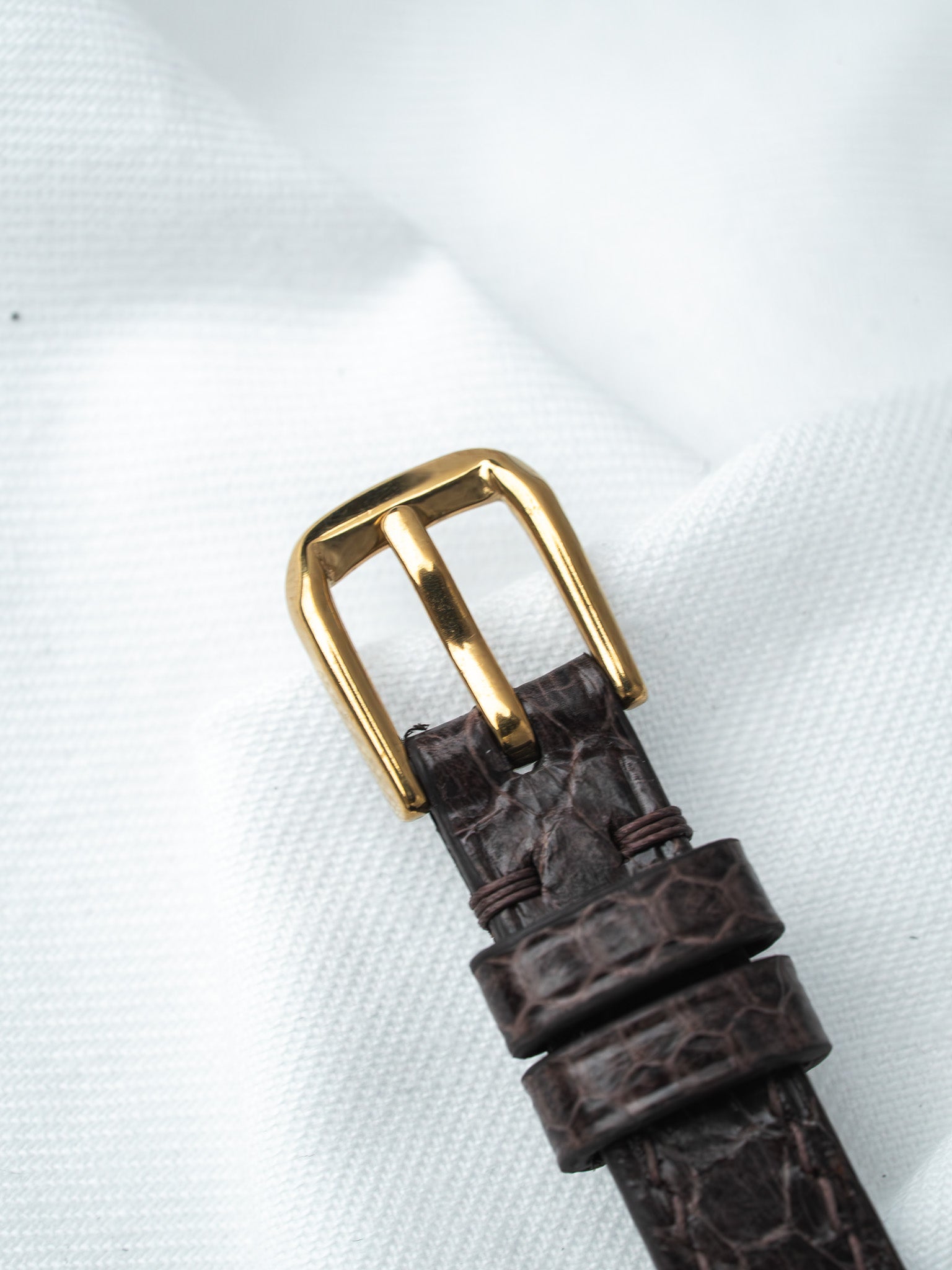 Brown alligator leather watch strap with gold buckle on white fabric