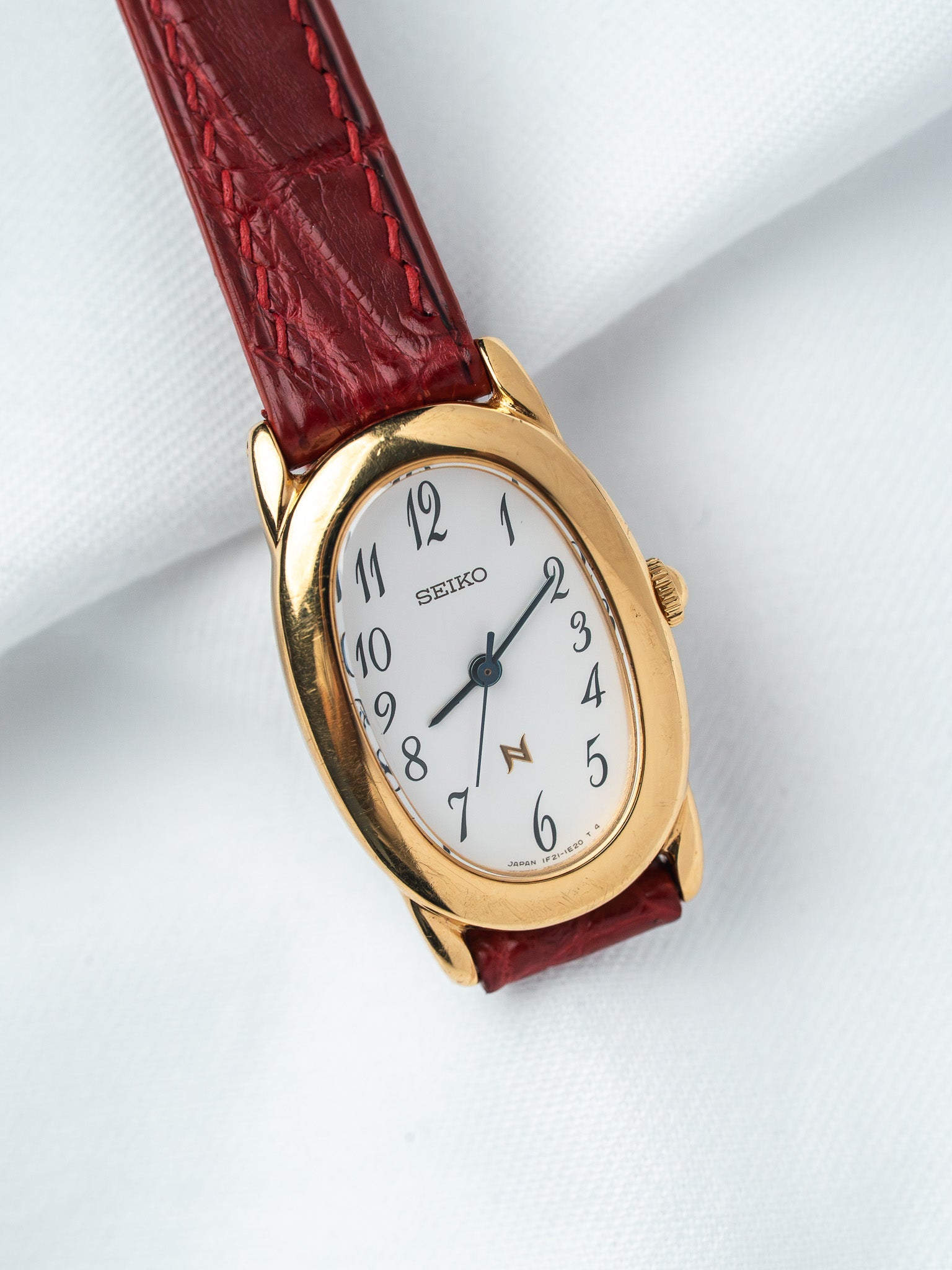 Seiko vintage watch with gold case, white dial, and red leather strap on white background