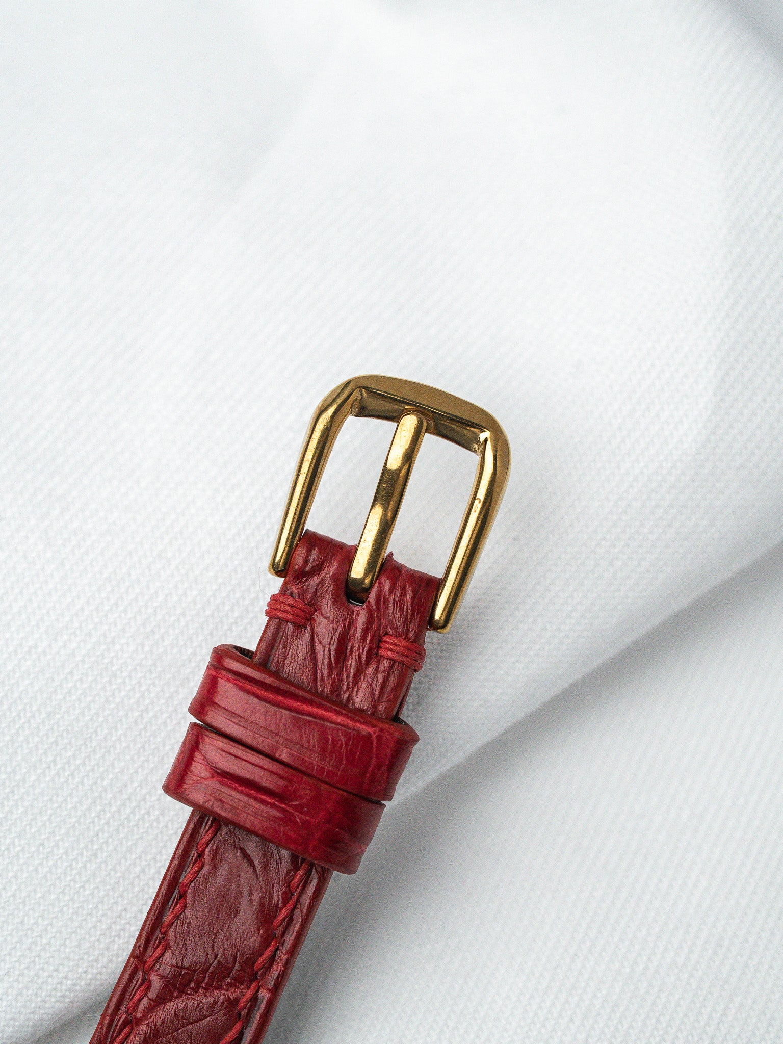 Red alligator leather watch strap with gold buckle on white fabric