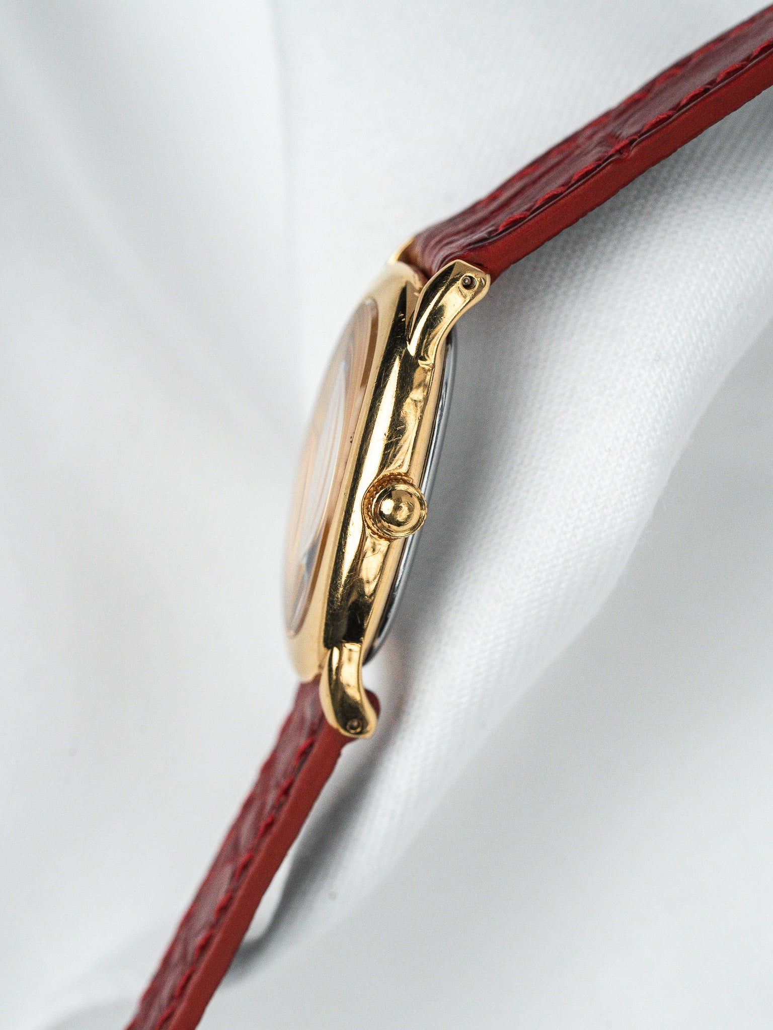Vintage Cartier watch with gold case and red leather strap on white fabric