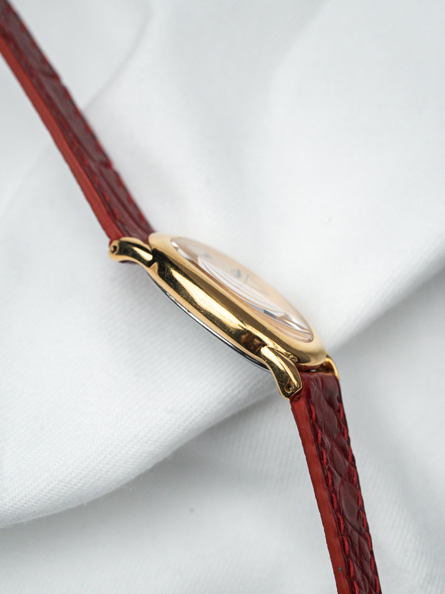 Vintage Cartier watch with gold case and red leather strap on white fabric
