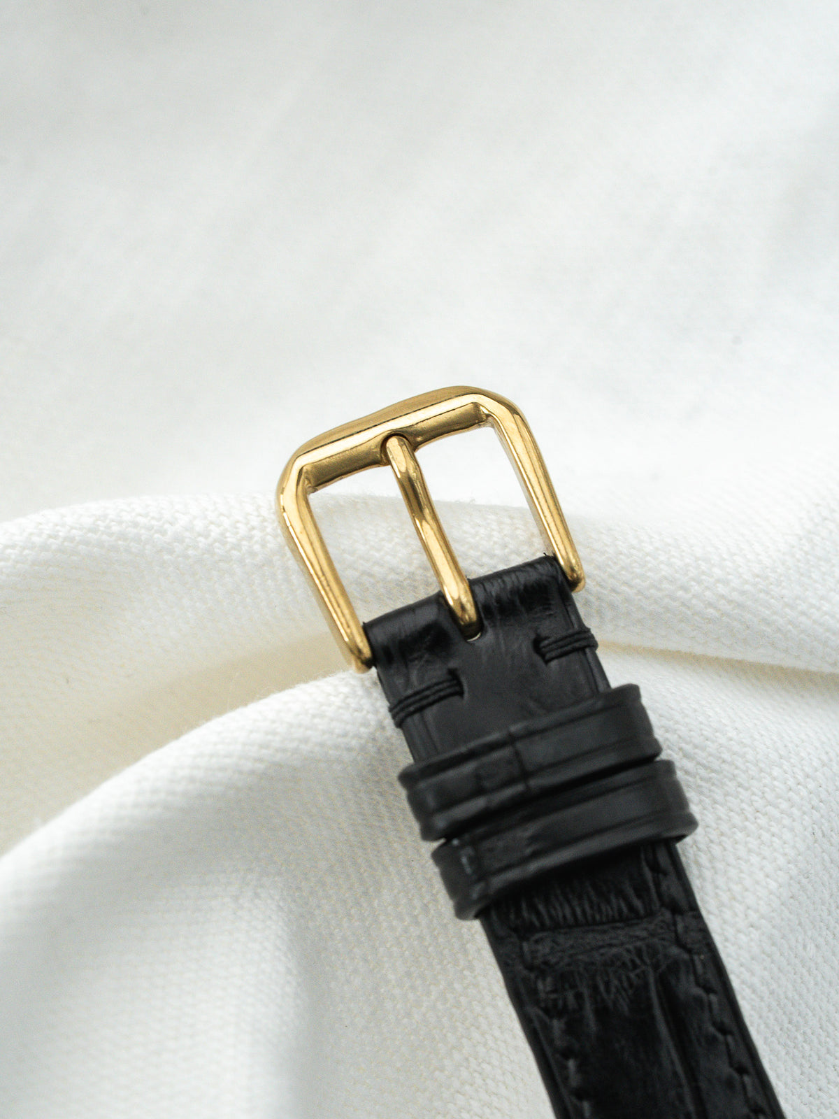 Black alligator leather watch strap with gold buckle on white fabric