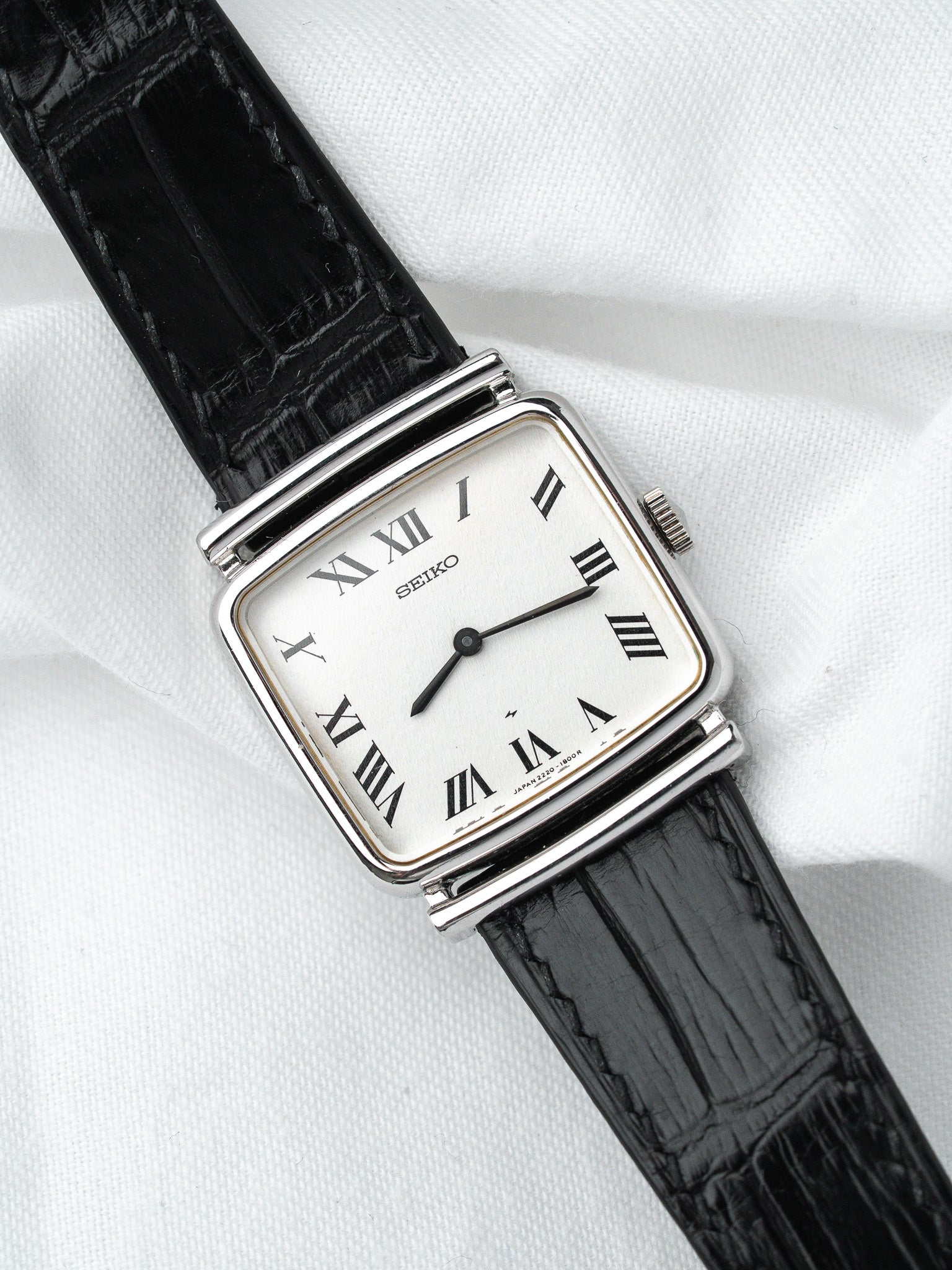 Seiko vintage watch with white dial, Roman numerals, black leather strap on white fabric