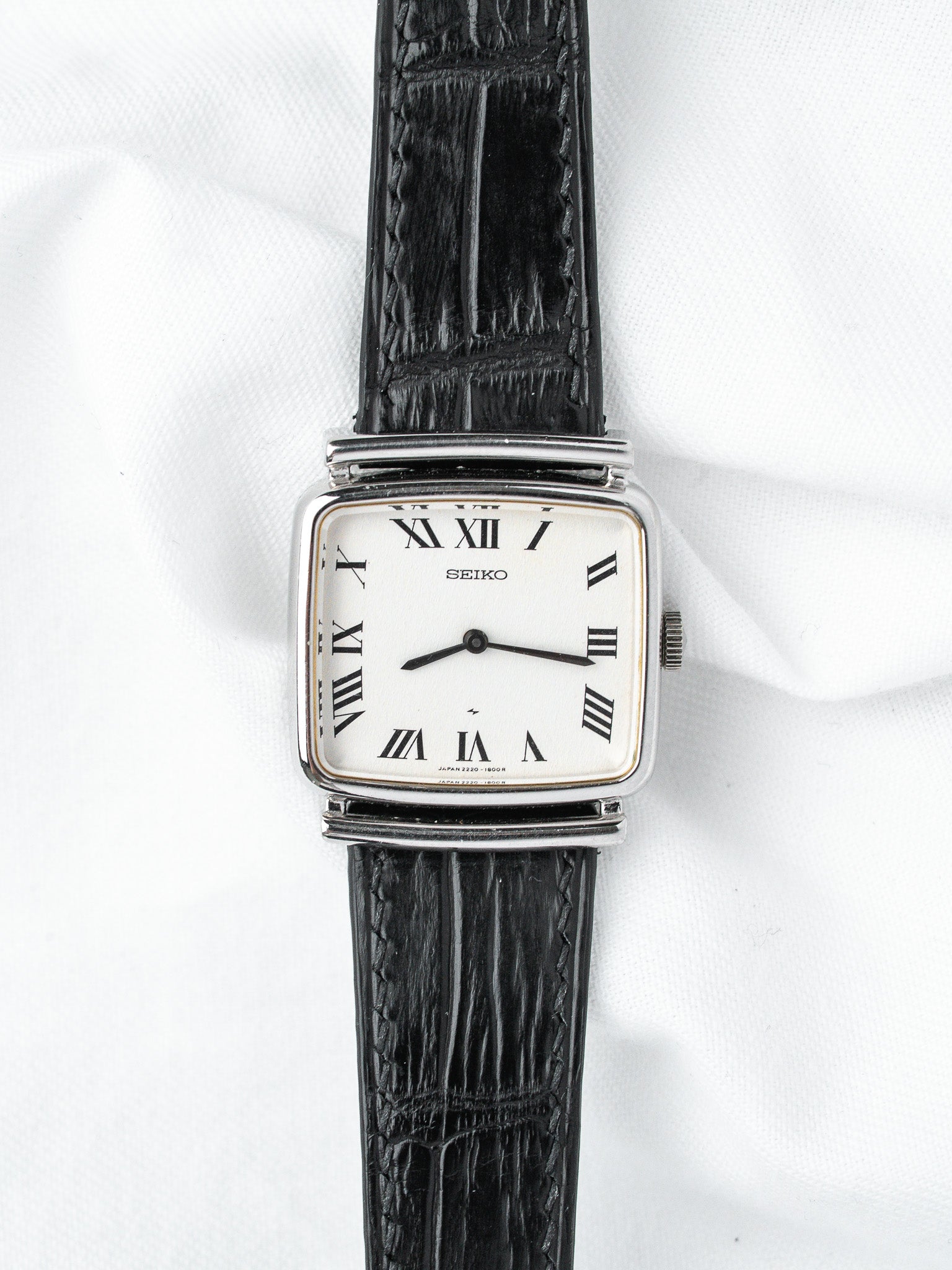 Seiko vintage watch with white dial, Roman numerals, black leather strap on white background