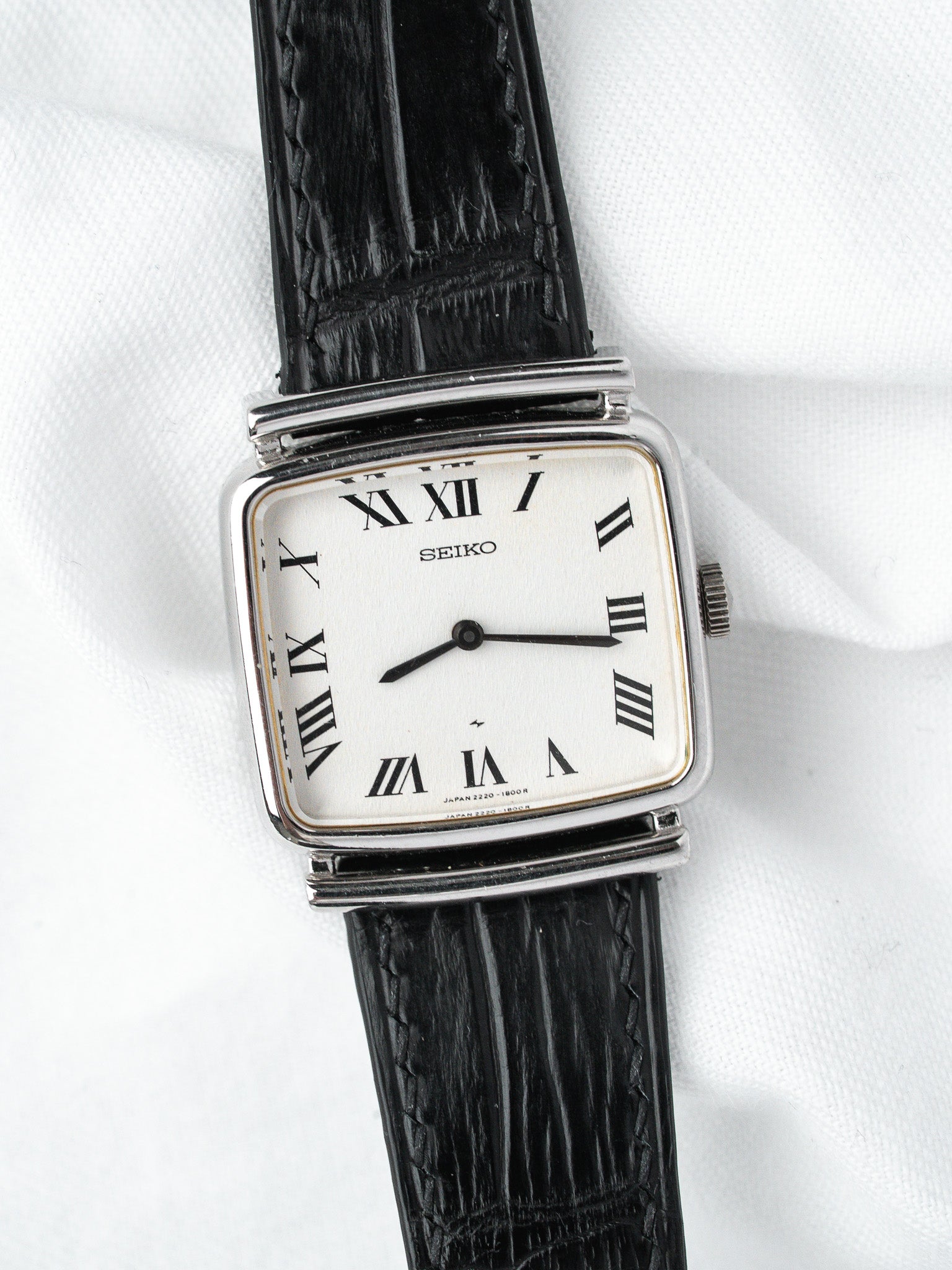 Seiko vintage watch with white dial, Roman numerals, black leather strap on white background