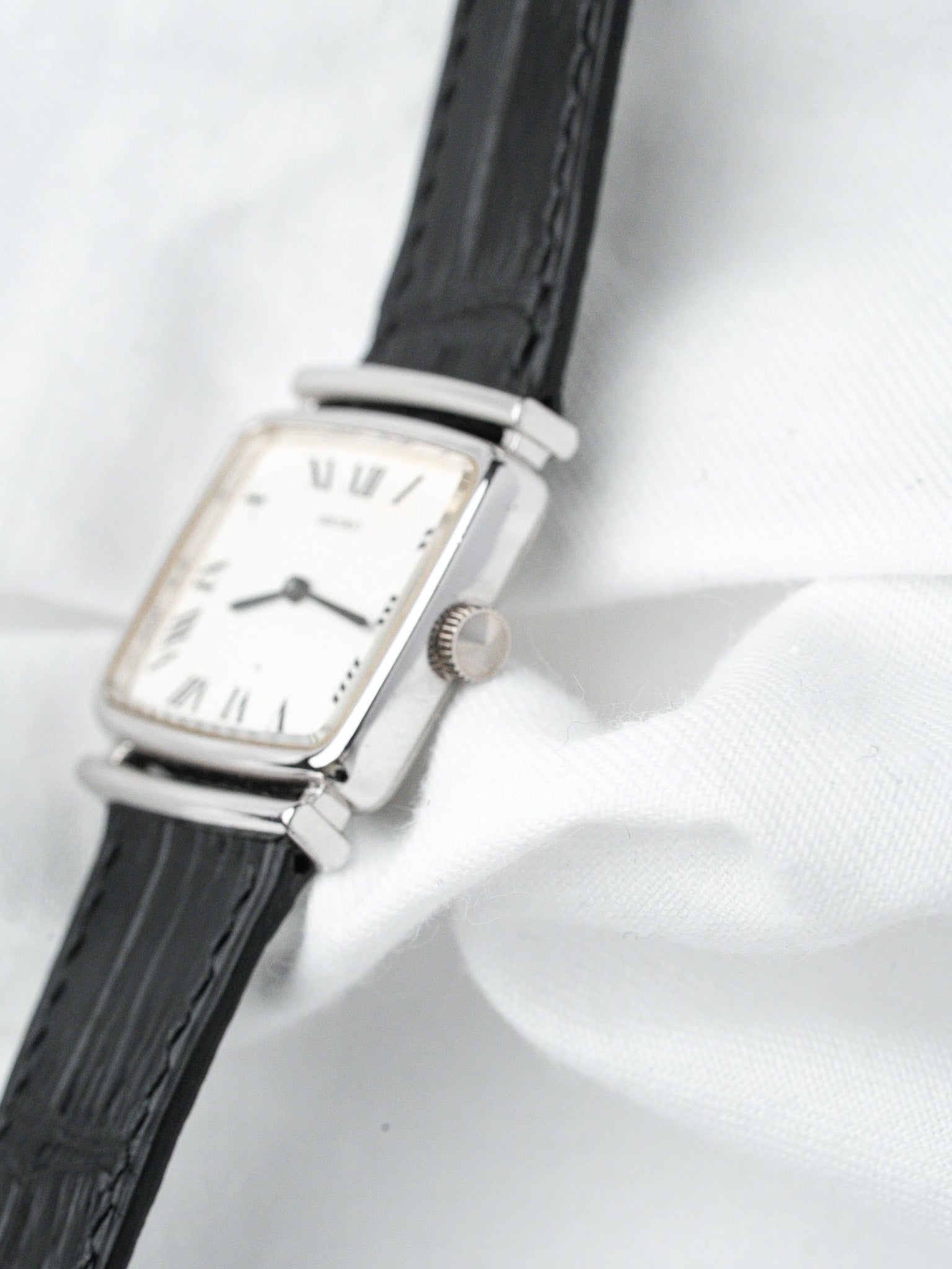 Vintage Cartier Tank watch with white dial, Roman numerals, black leather strap on white fabric
