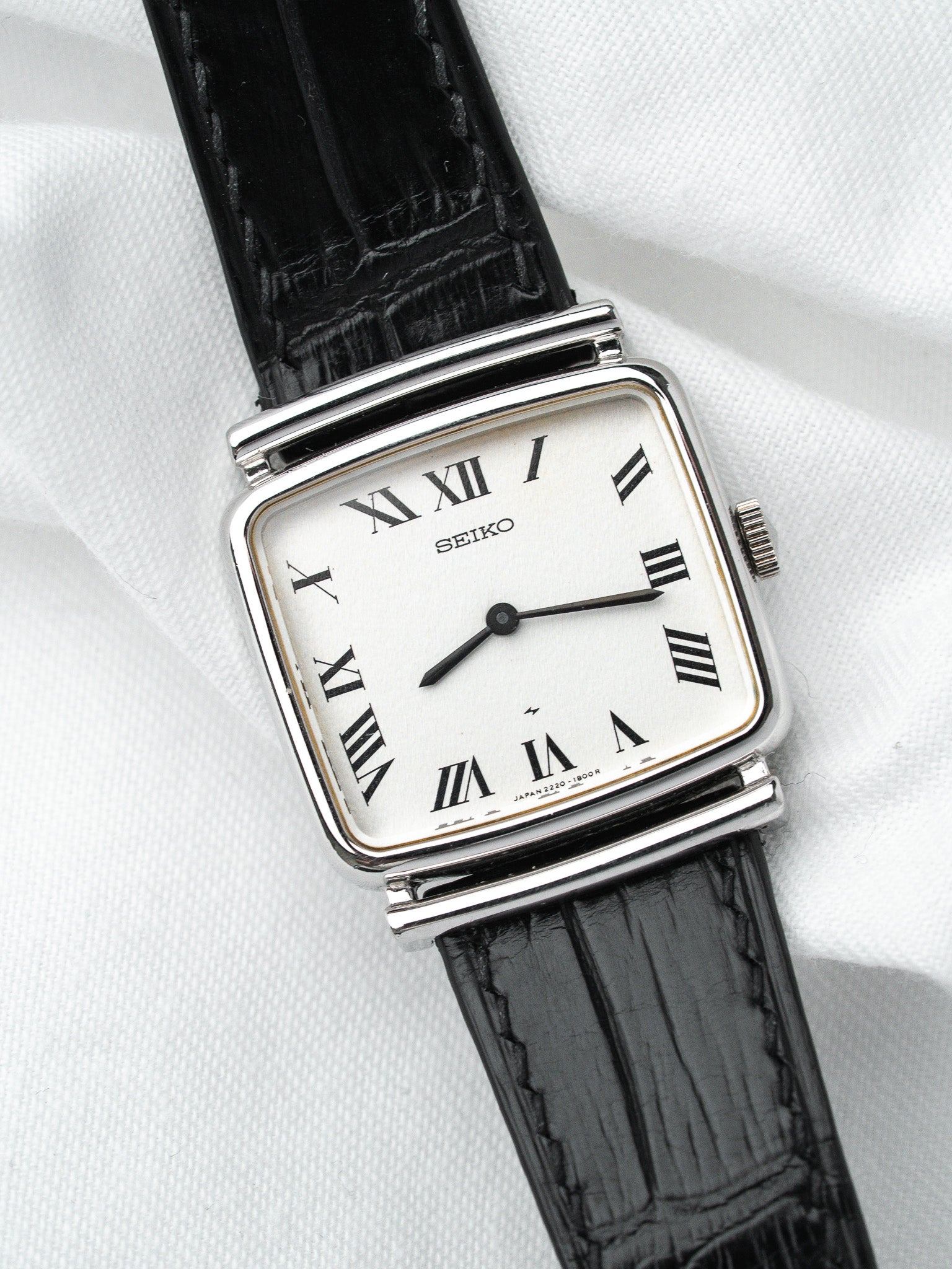 Seiko vintage watch with white dial, Roman numerals, black leather strap on white fabric