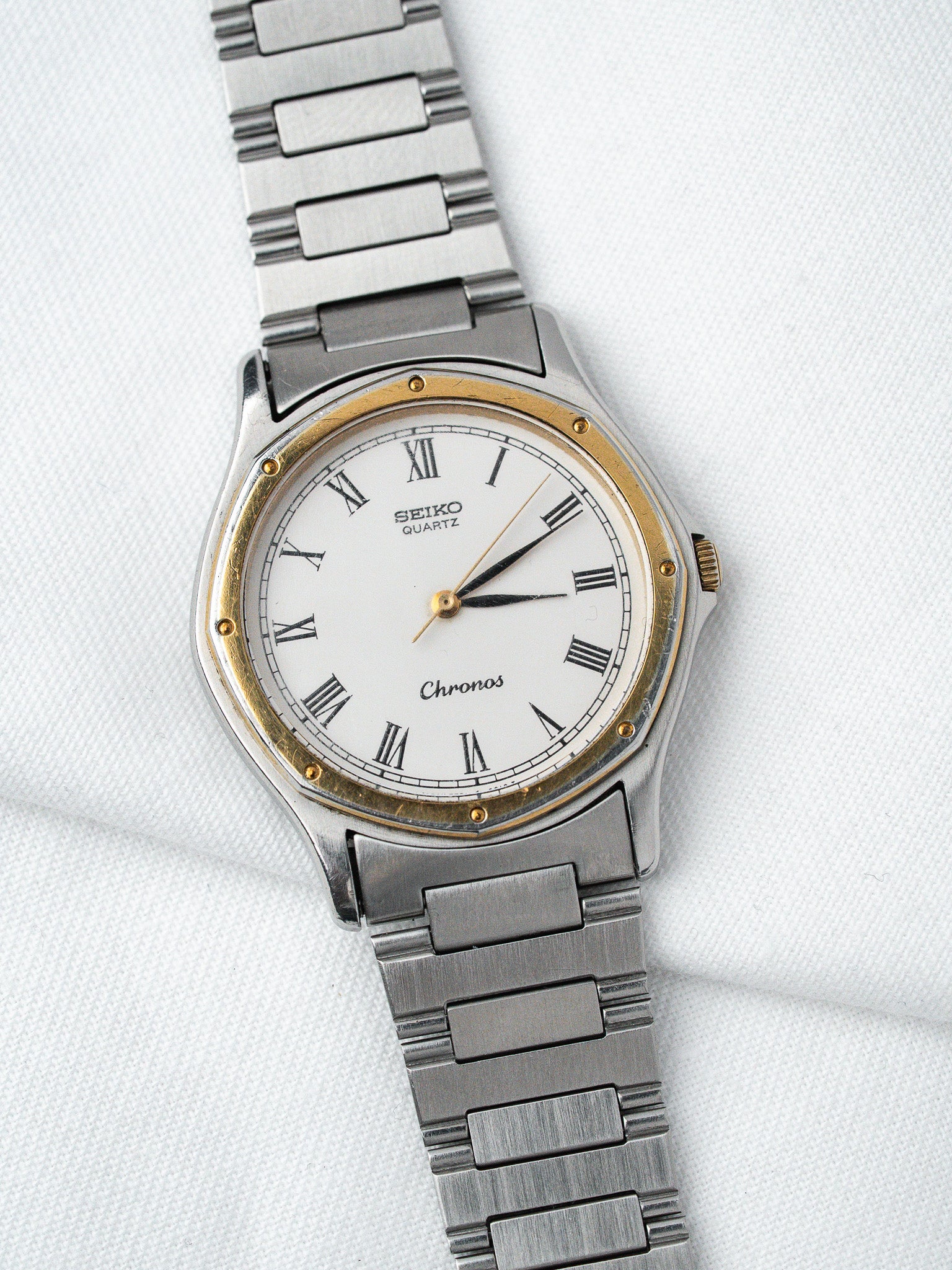 Seiko Chronos vintage quartz watch with white dial, Roman numerals, gold accents, and steel bracelet
