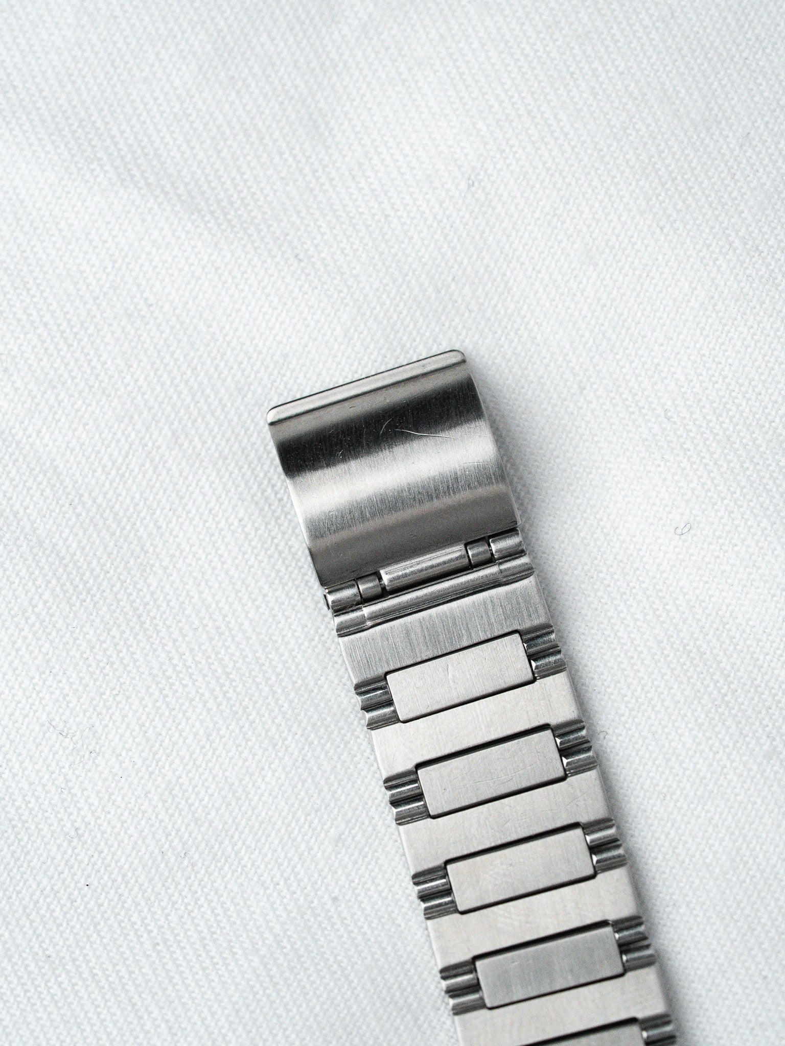 Stainless steel watch bracelet with brushed finish and deployant clasp on white fabric