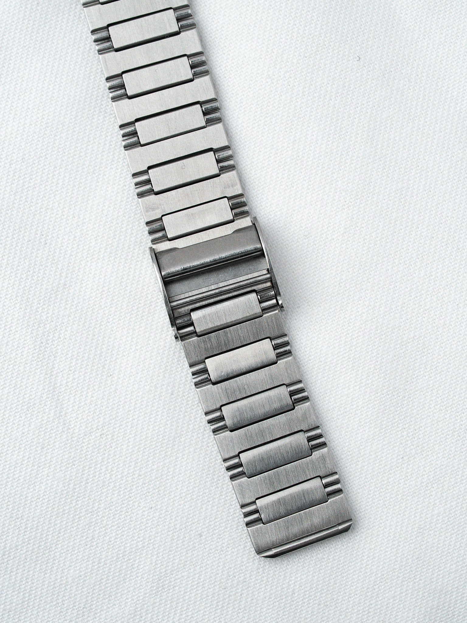 Stainless steel watch bracelet with brushed finish, laid flat on white fabric background