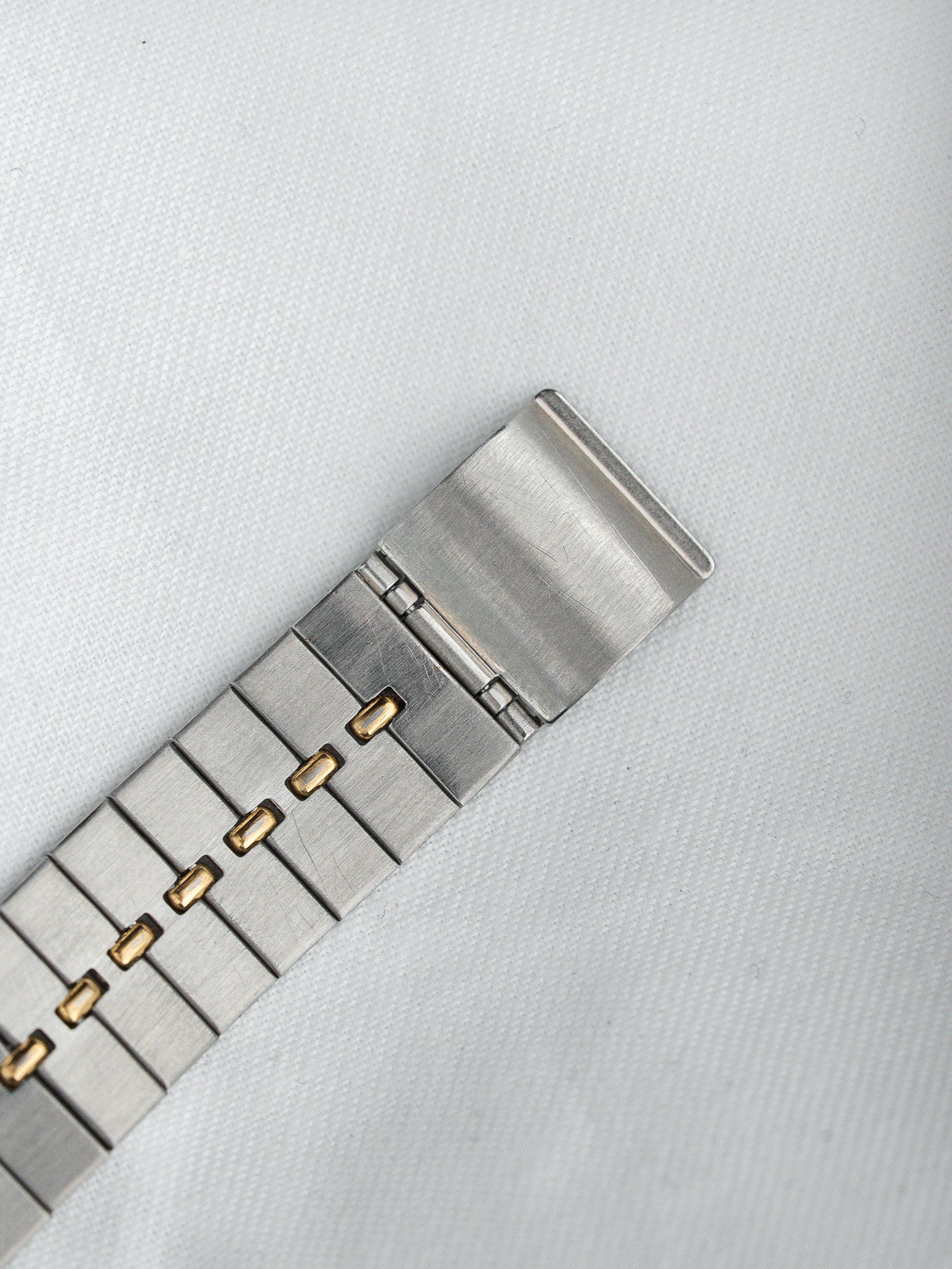 Stainless steel watch bracelet with gold accents, brushed finish, on neutral background
